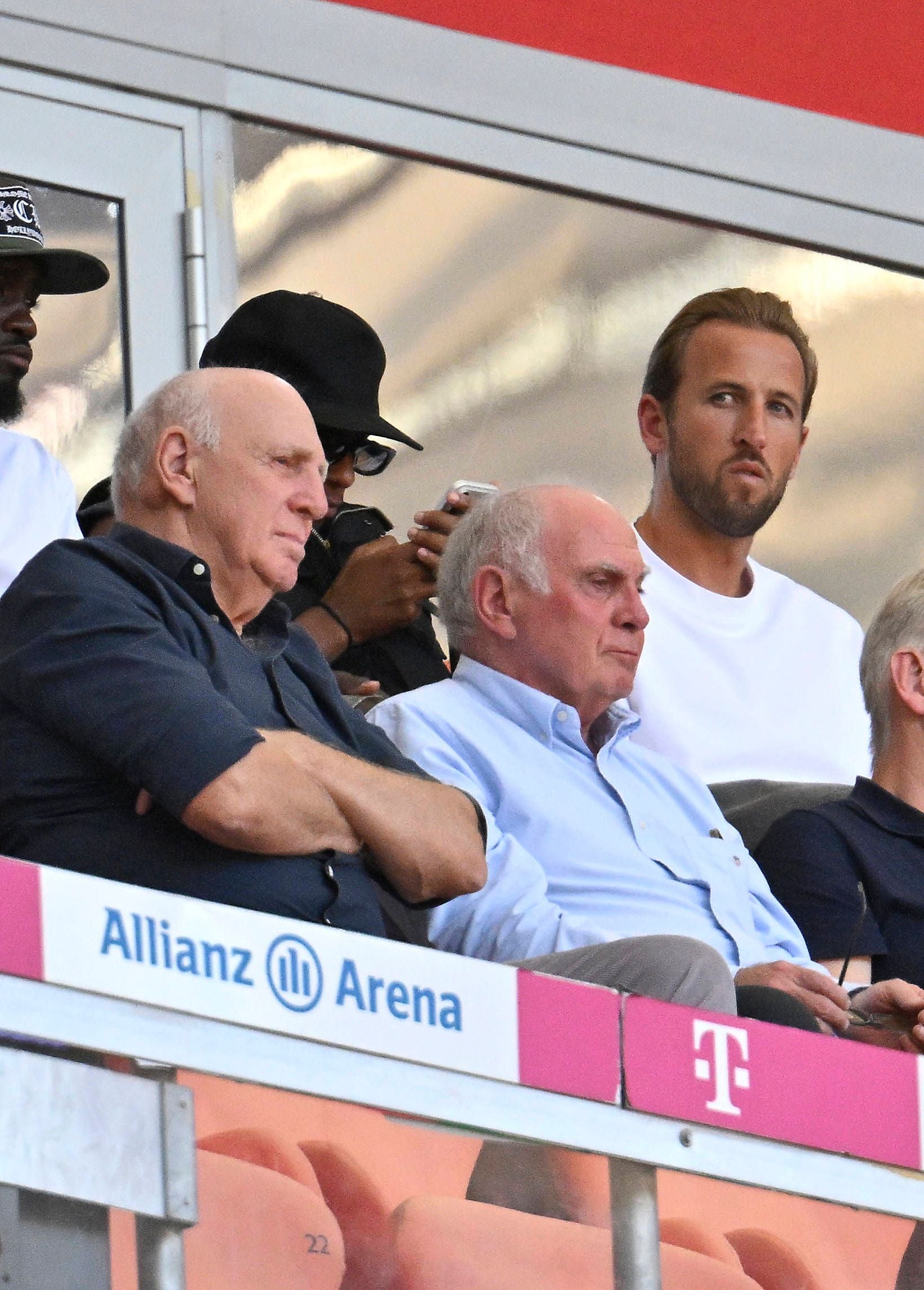 Harry Kane, Uli Hoeneß und Dieter Hoeneß sitzen auf der Tribüne der Allianz Arena beim Fußballspiel.