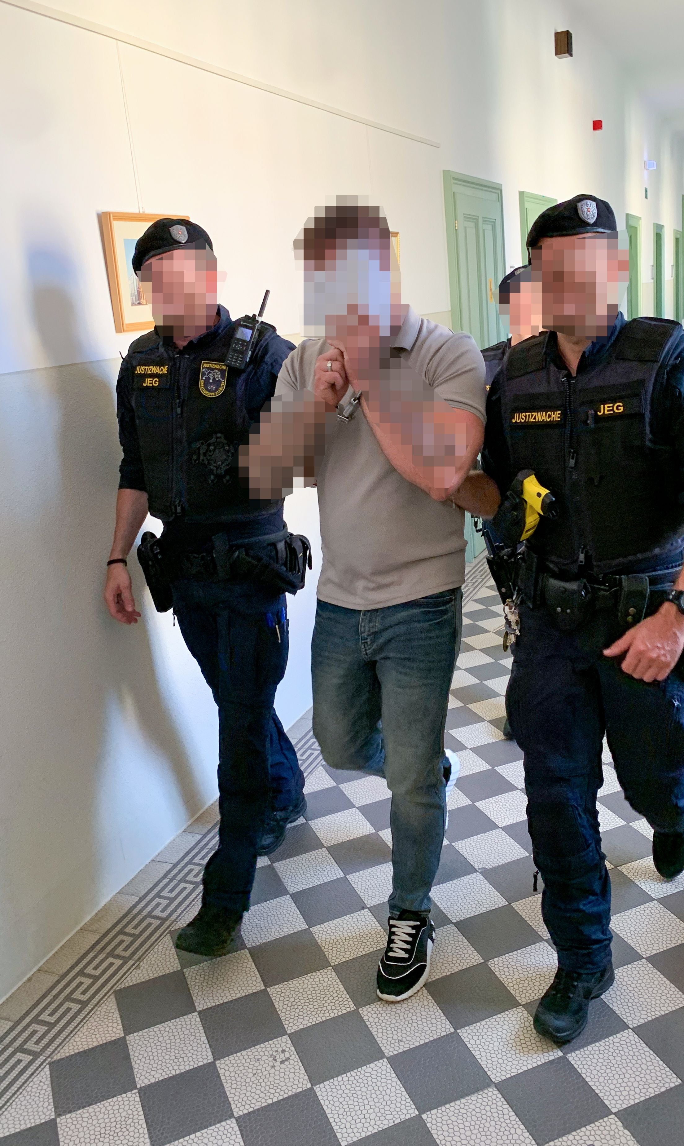 Ein Angeklagter wird von zwei Justizbeamten durch einen Gerichtsflur geführt.