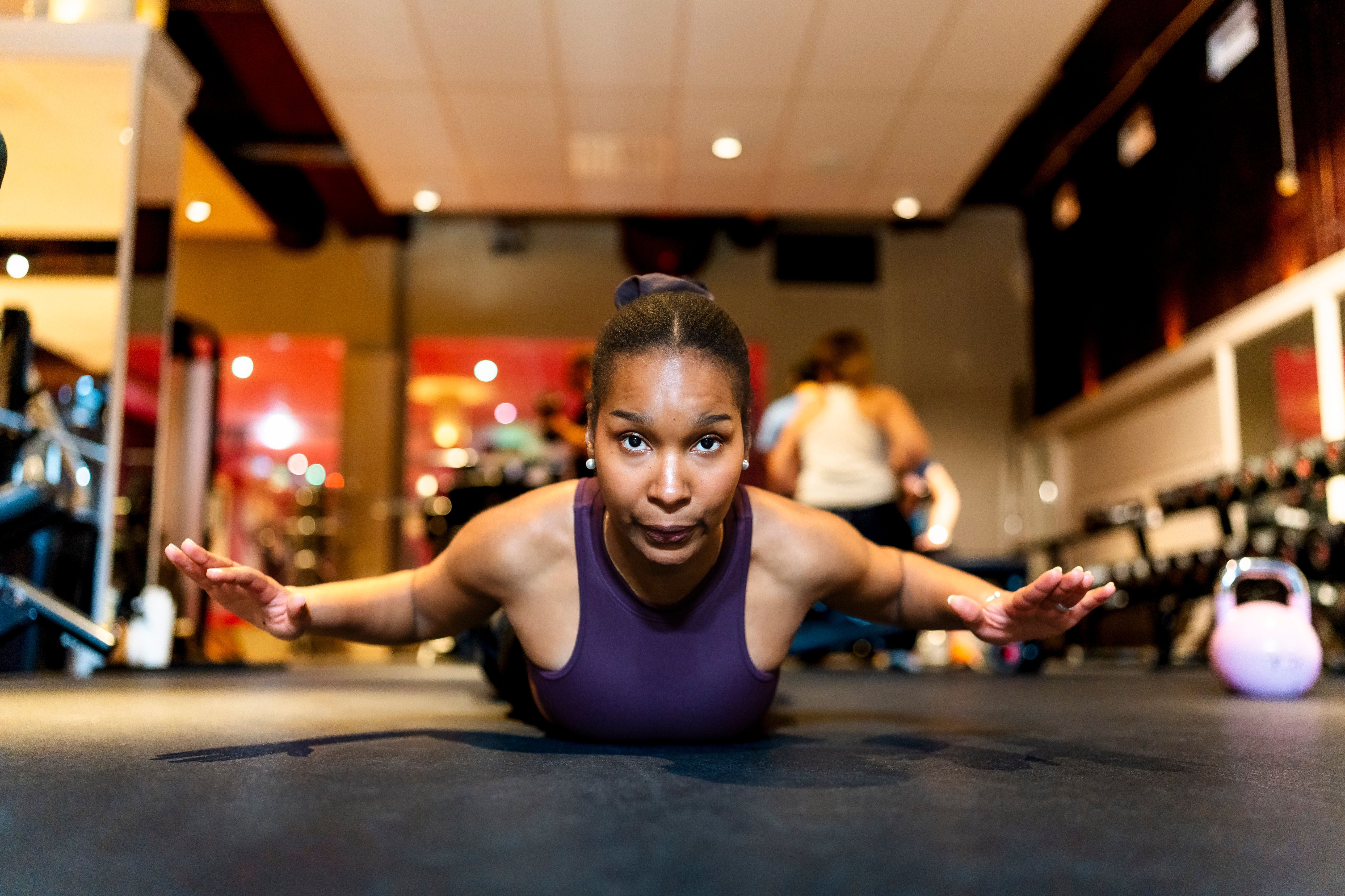 Frau macht eine Fitnessübung auf dem Boden im Fitnessstudio, Arme seitlich ausgestreckt.