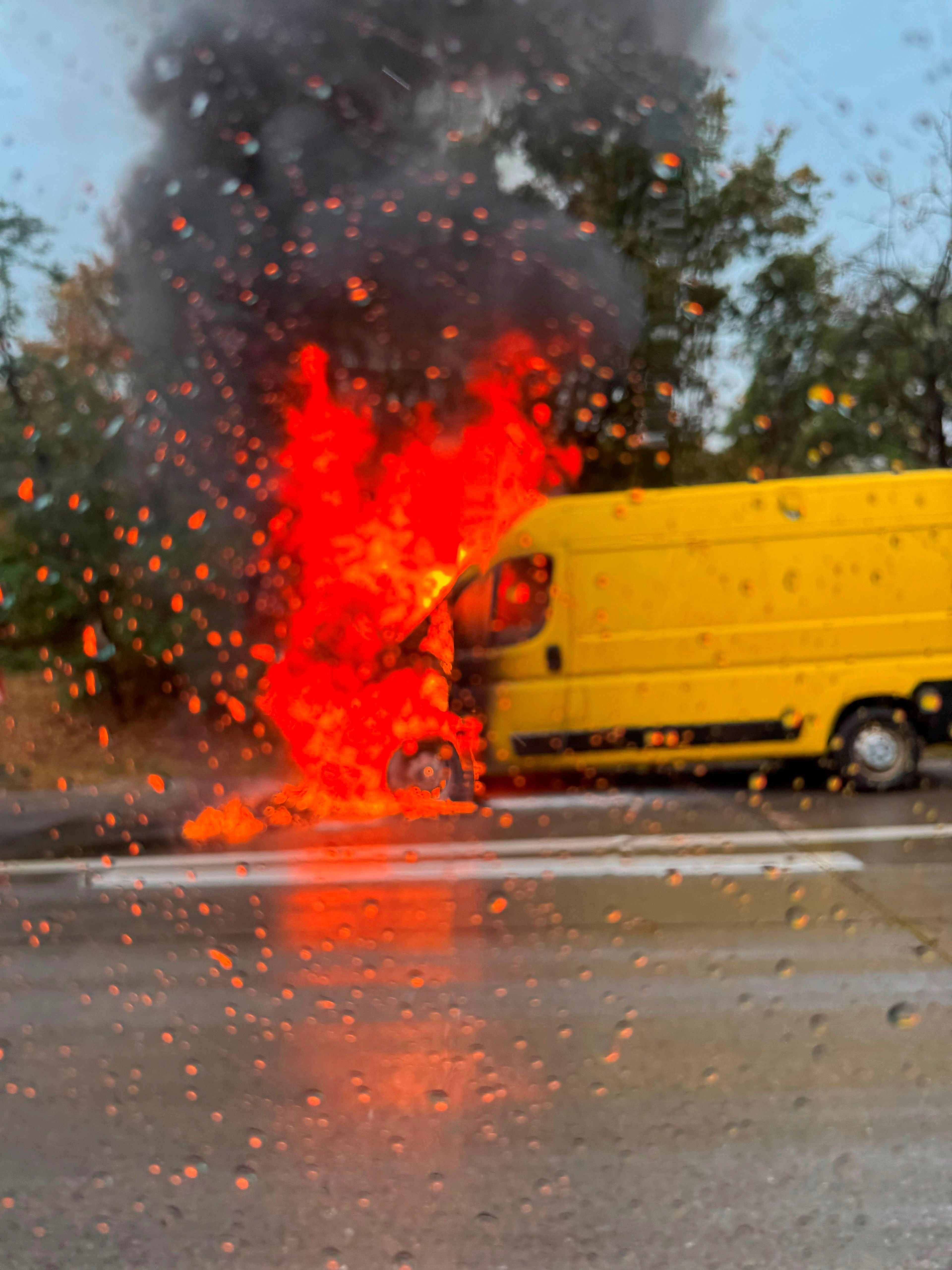 Ein gelber Lieferwagen steht brennend mit starker Rauchentwicklung am Straßenrand.
