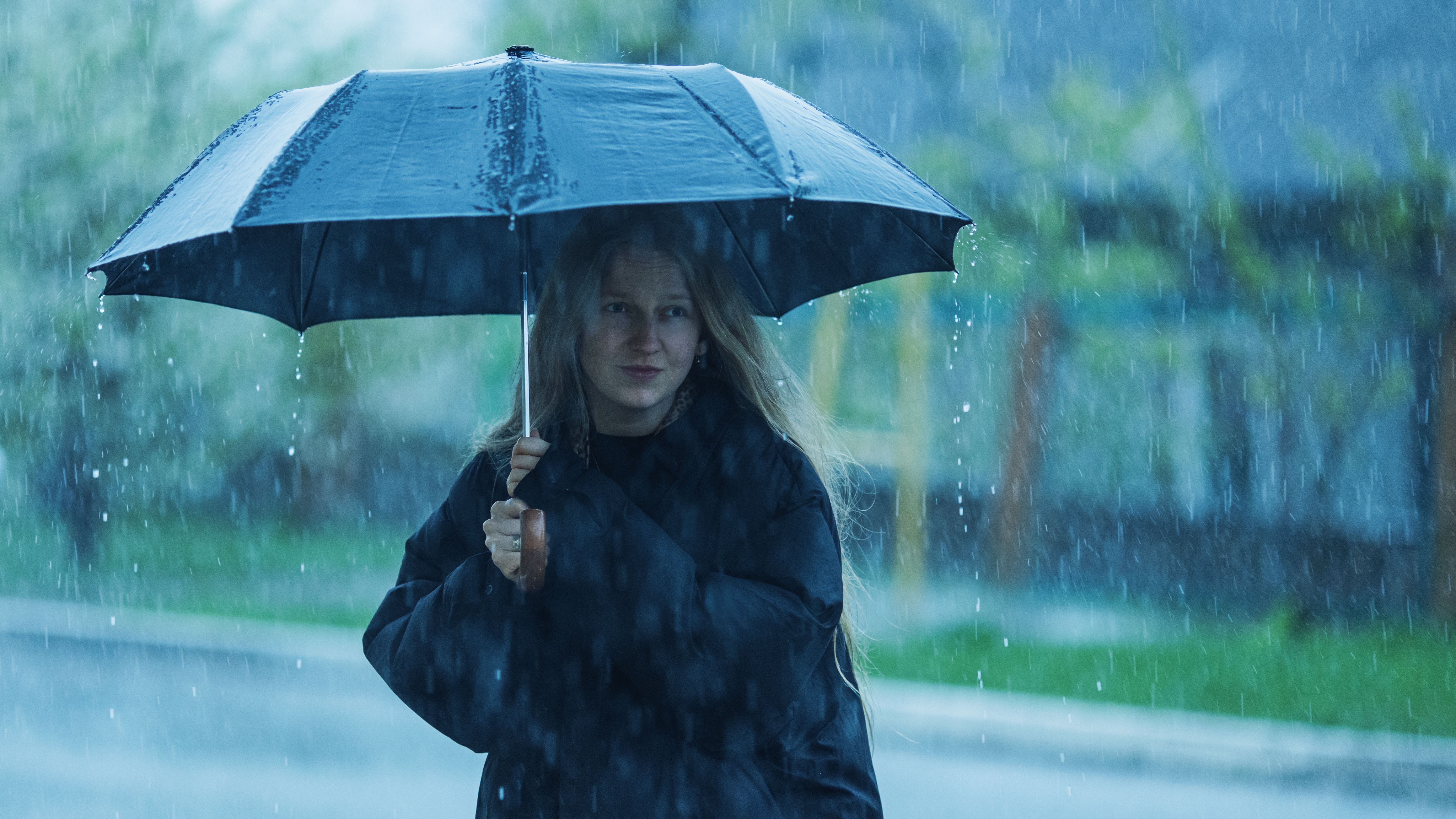 Frau mit langem Haar steht unter einem schwarzen Regenschirm im strömenden Regen.