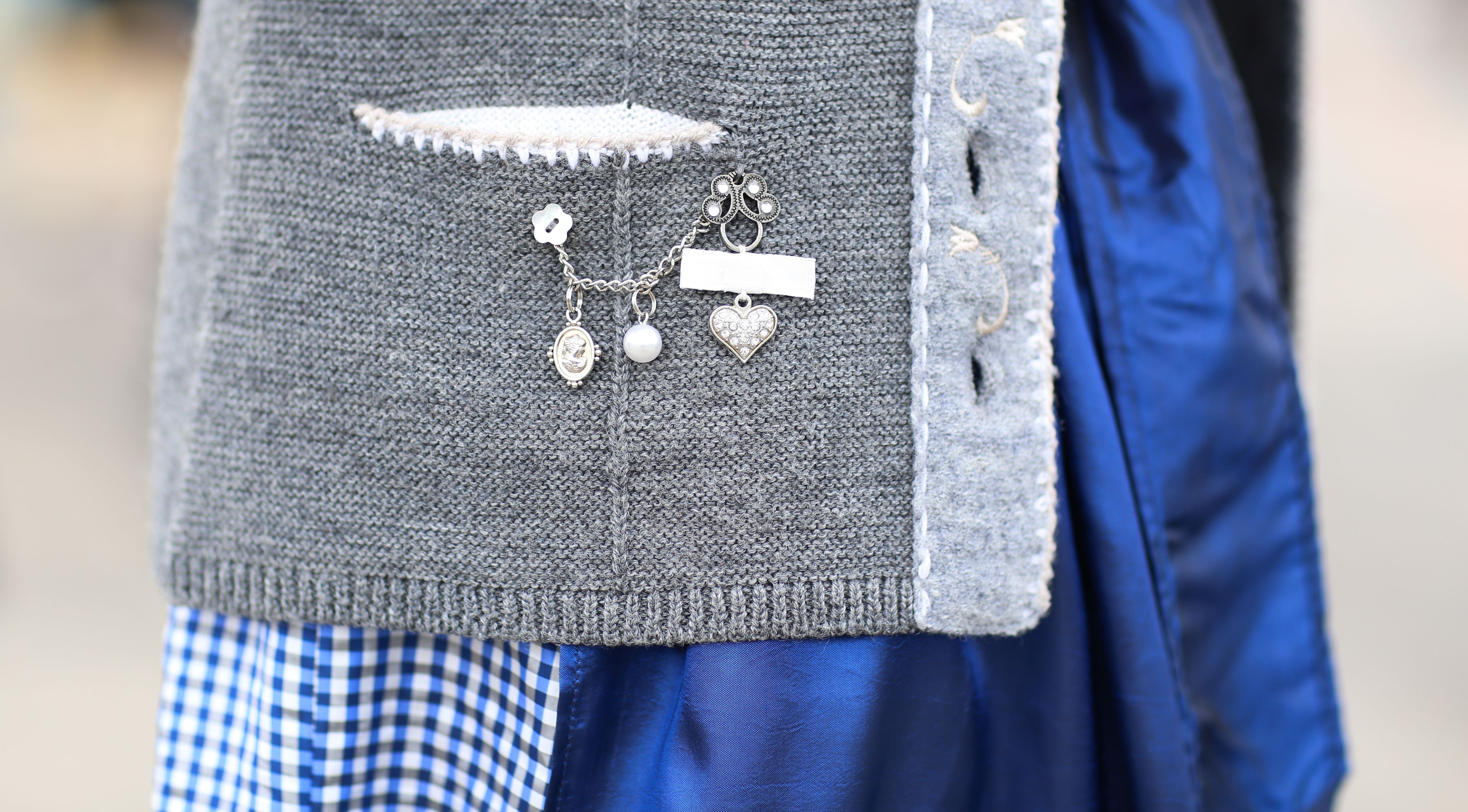 Detail eines grauen Dirndl-Mieders mit Anstecker, darunter blauer und kariert-blauer Rockstoff.