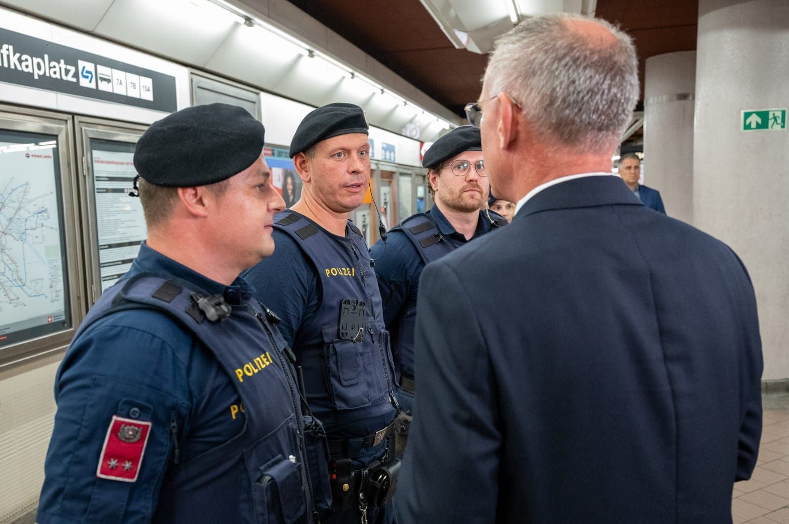 Drei Polizisten sprechen mit einem Mann im Anzug in einer U-Bahn-Station.