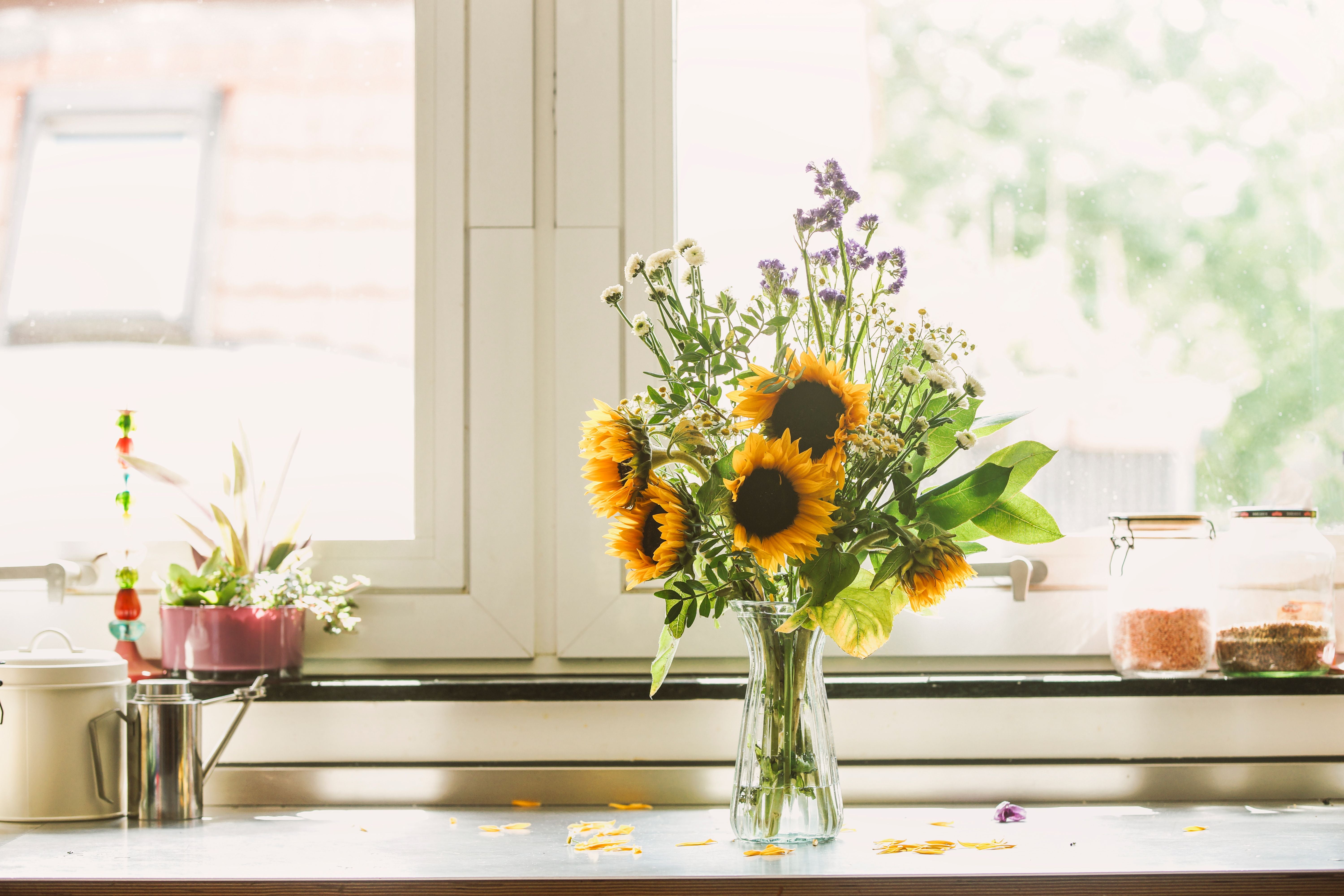 Ein Blumenstrauß mit Sonnenblumen steht auf einem Küchentisch vor einem Fenster.