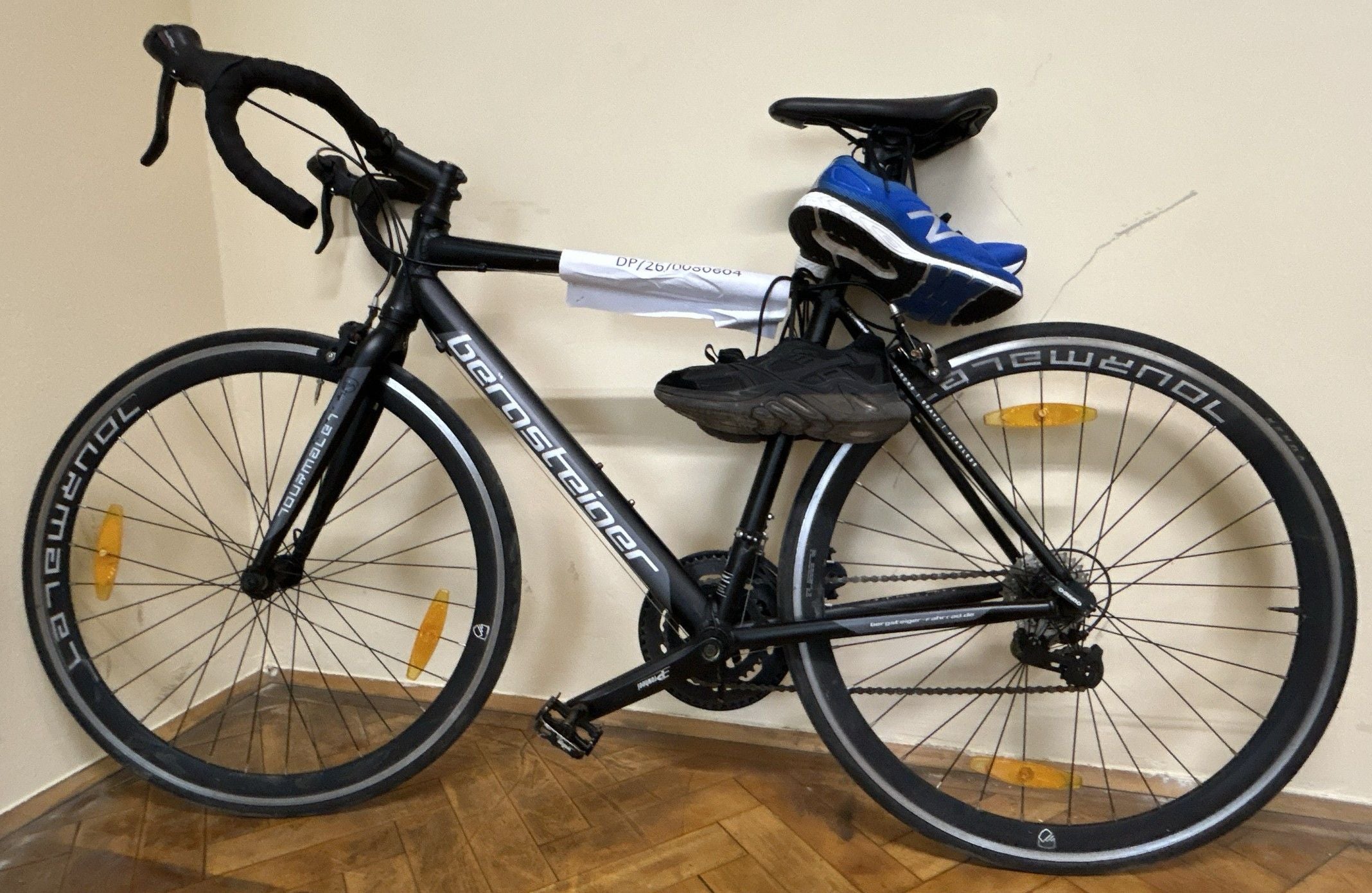 Ein Rennrad lehnt an einer Wand, auf dem Sattel hängen ein blau und ein schwarzer Sportschuh.