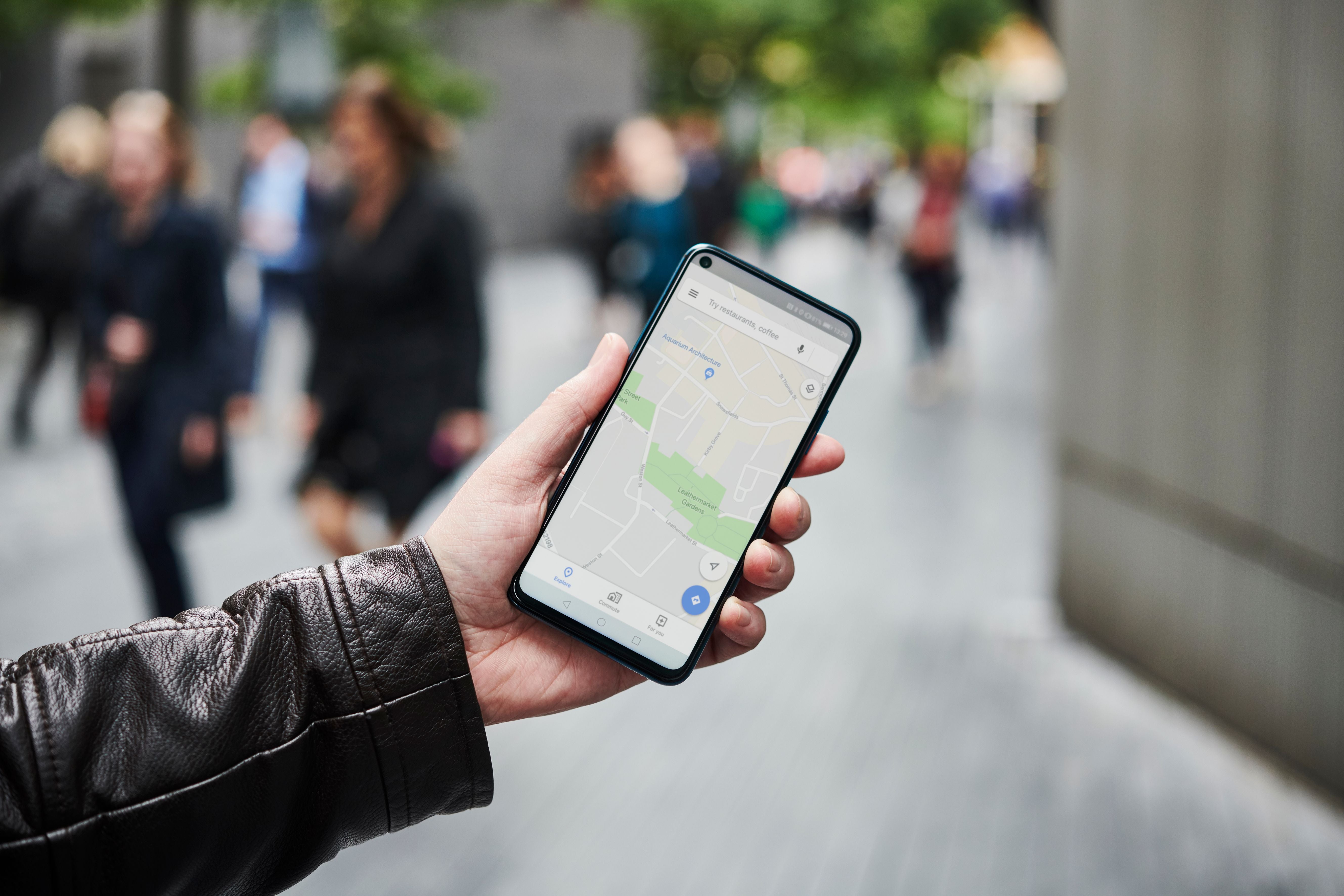 Ein Mann hält ein Smartphone mit geöffneter Google Maps App auf einer belebten Straße.