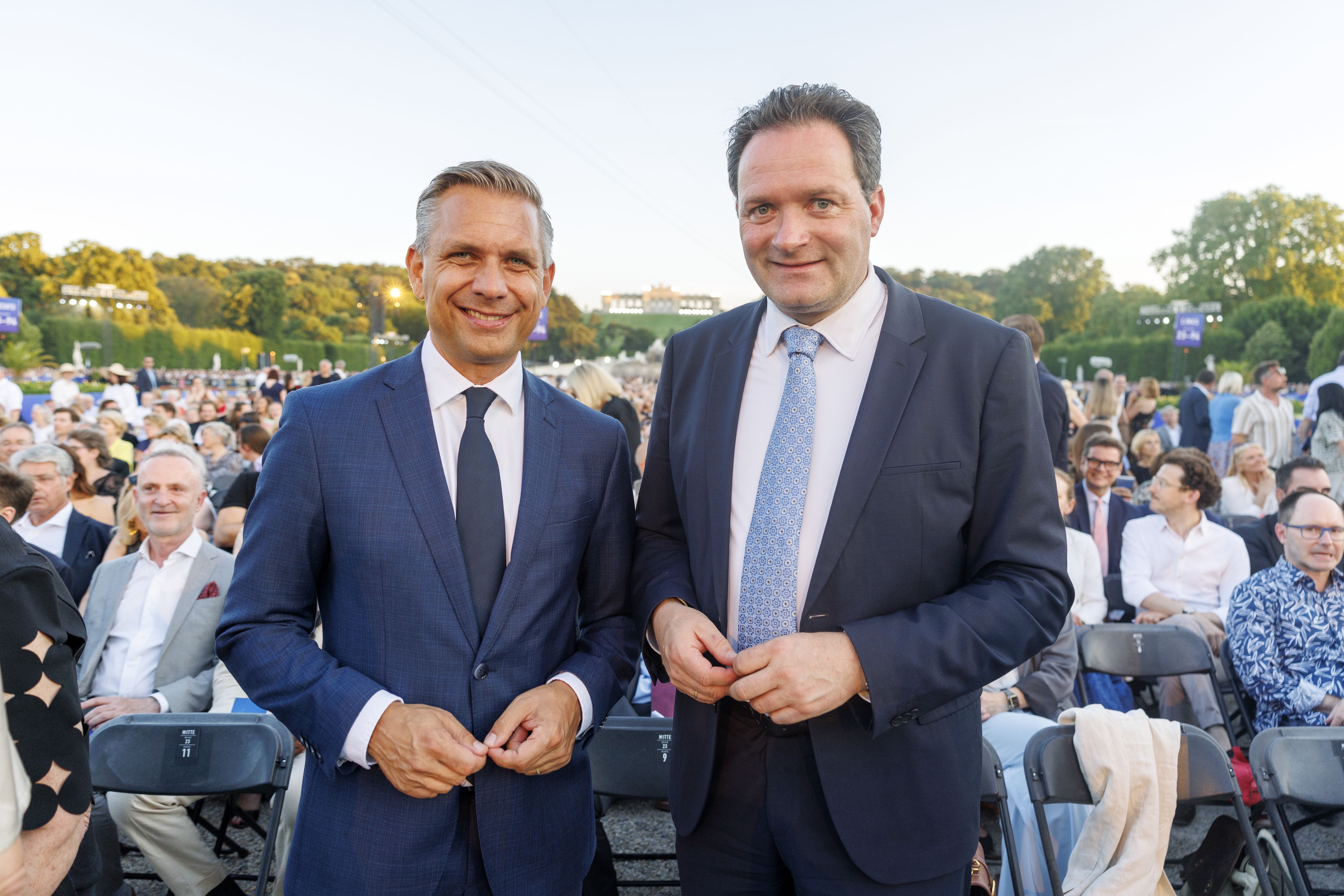 Zwei Männer im Anzug stehen beim Sommernachtskonzert im Schlosspark Schönbrunn, Publikum im Hintergrund.