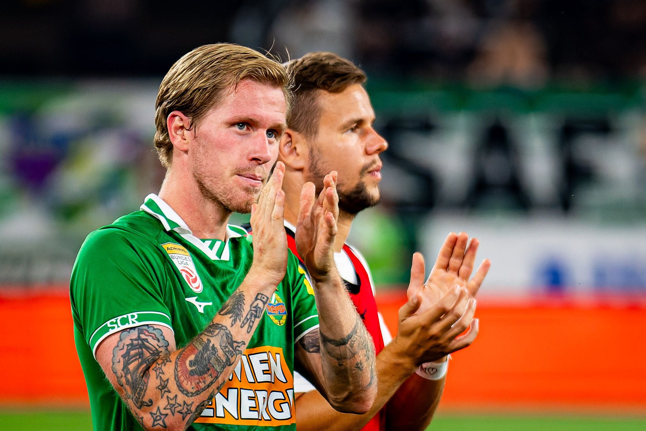 Zwei Fußballspieler im Rapid Wien-Trikot applaudieren nach dem Spiel auf dem Spielfeld.
