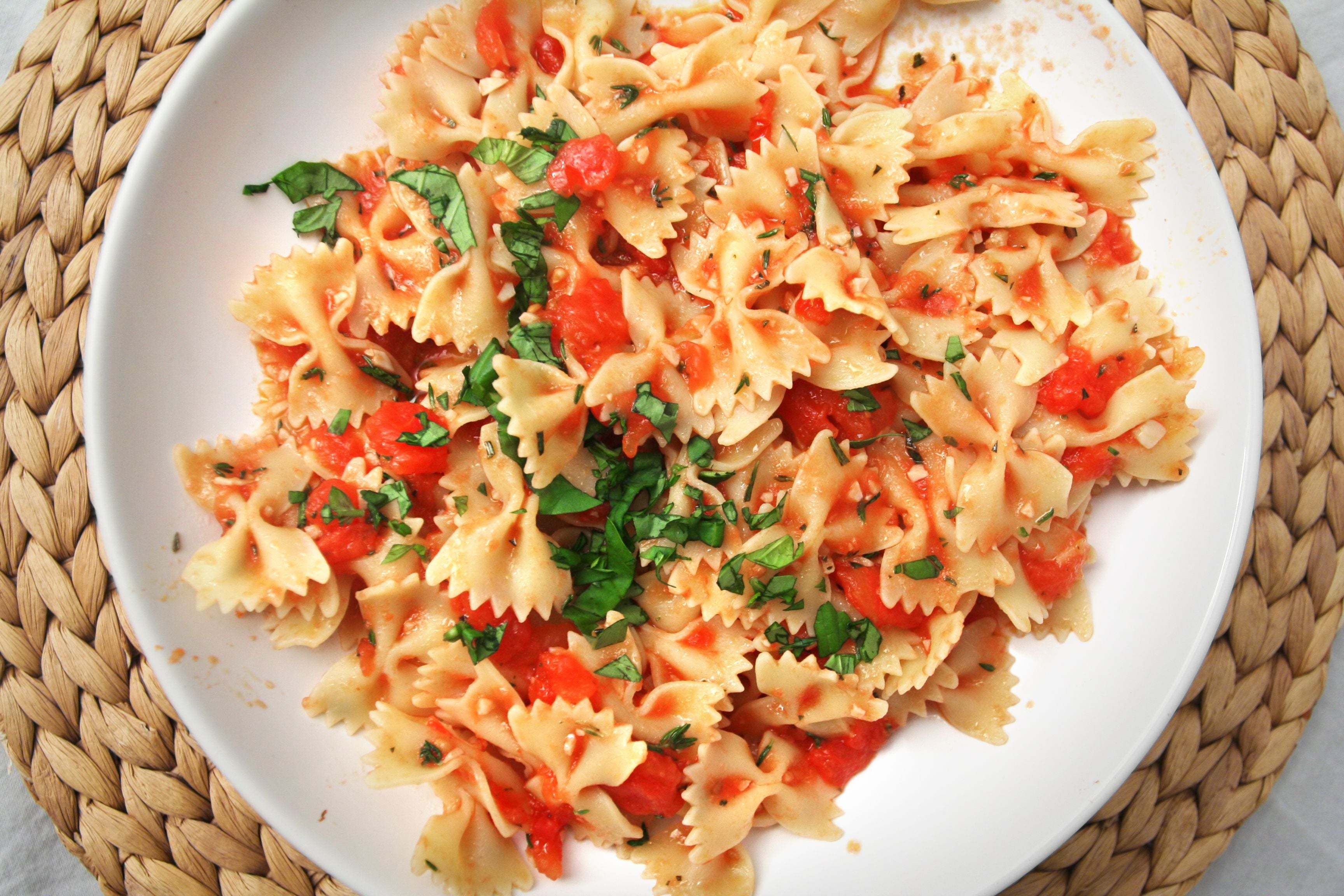 Farfalle-Nudeln mit Tomatensauce und frischen Kräutern auf einem weißen Teller.