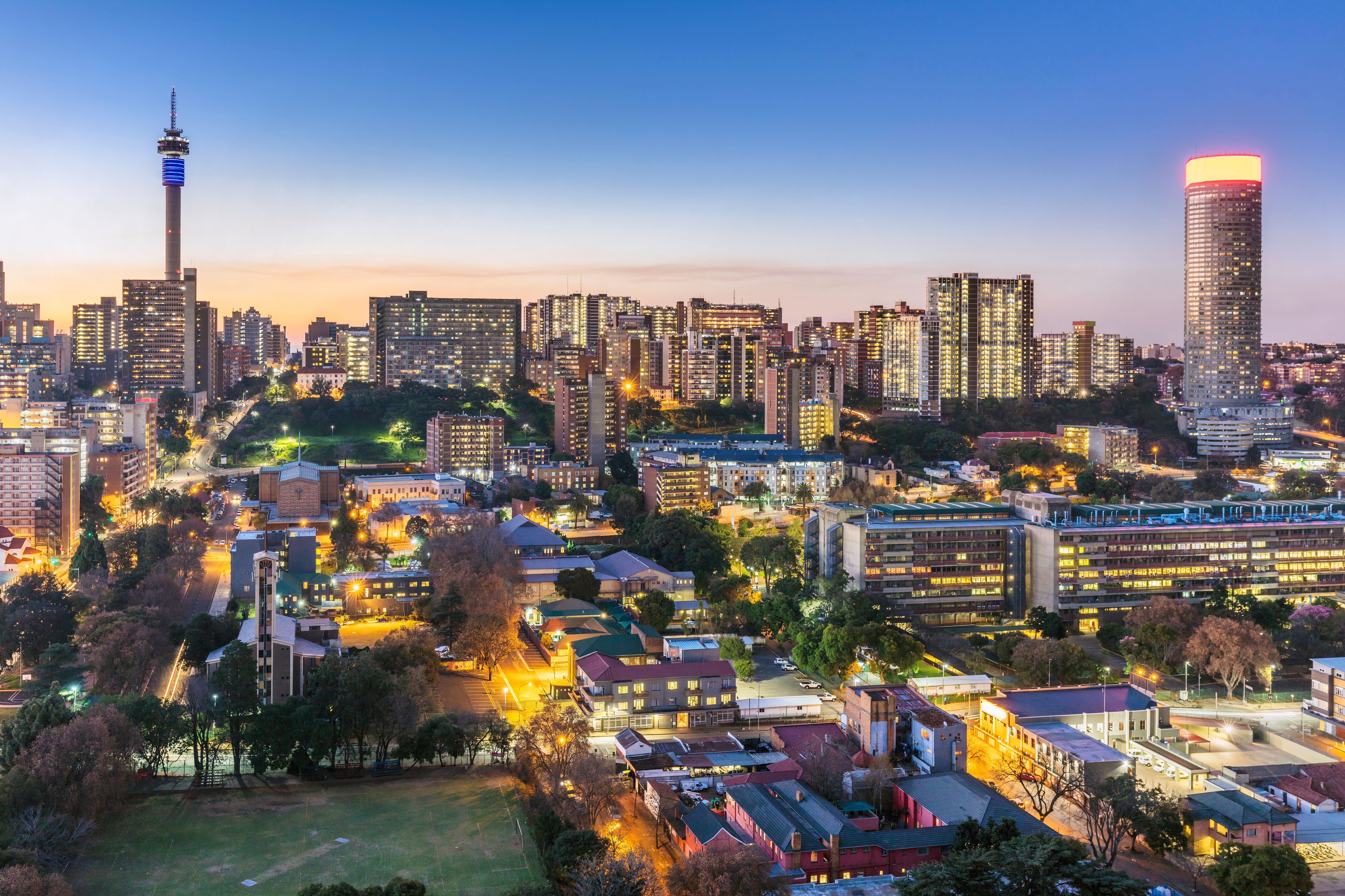 Johannesburg Skyline bei Sonnenuntergang mit Telkom-Turm und beleuchteten Hochhäusern.