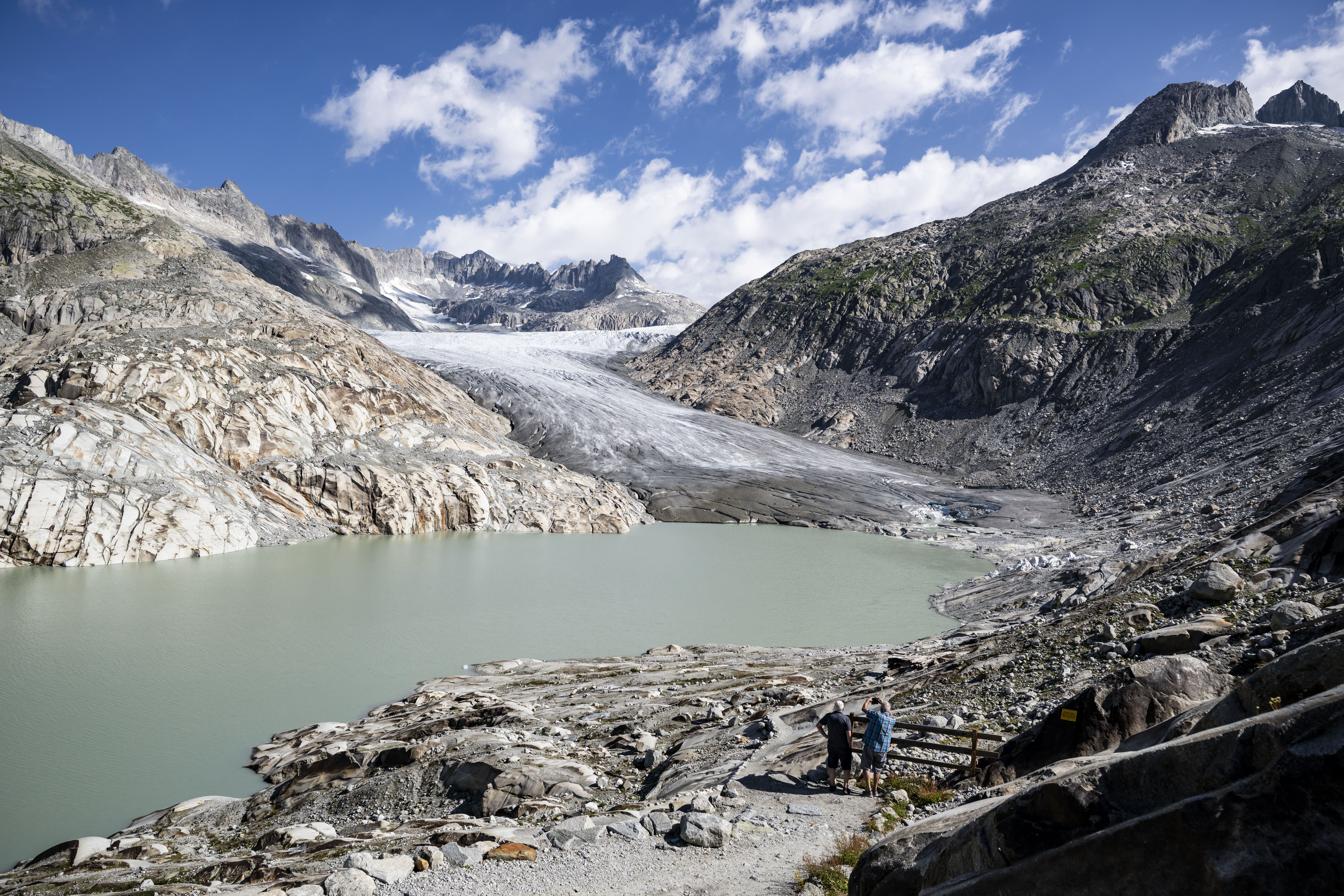 Zwei Touristen beobachten den Gletscherrückgang am Rhône-Gletscher in einer alpinen Landschaft.