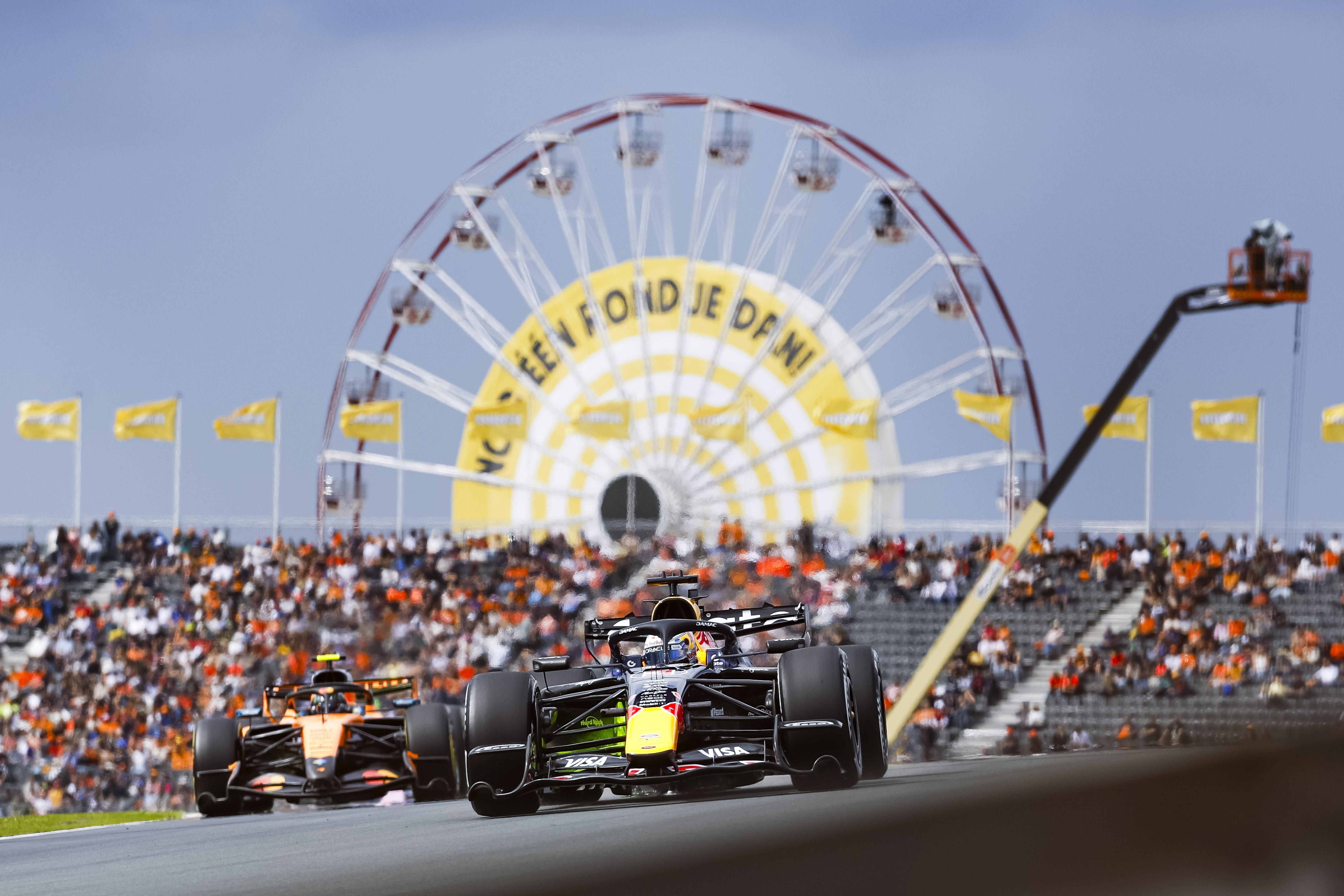 Zwei Formel-1-Autos fahren vor Zuschauern und einem Riesenrad auf der Rennstrecke in Zandvoort.