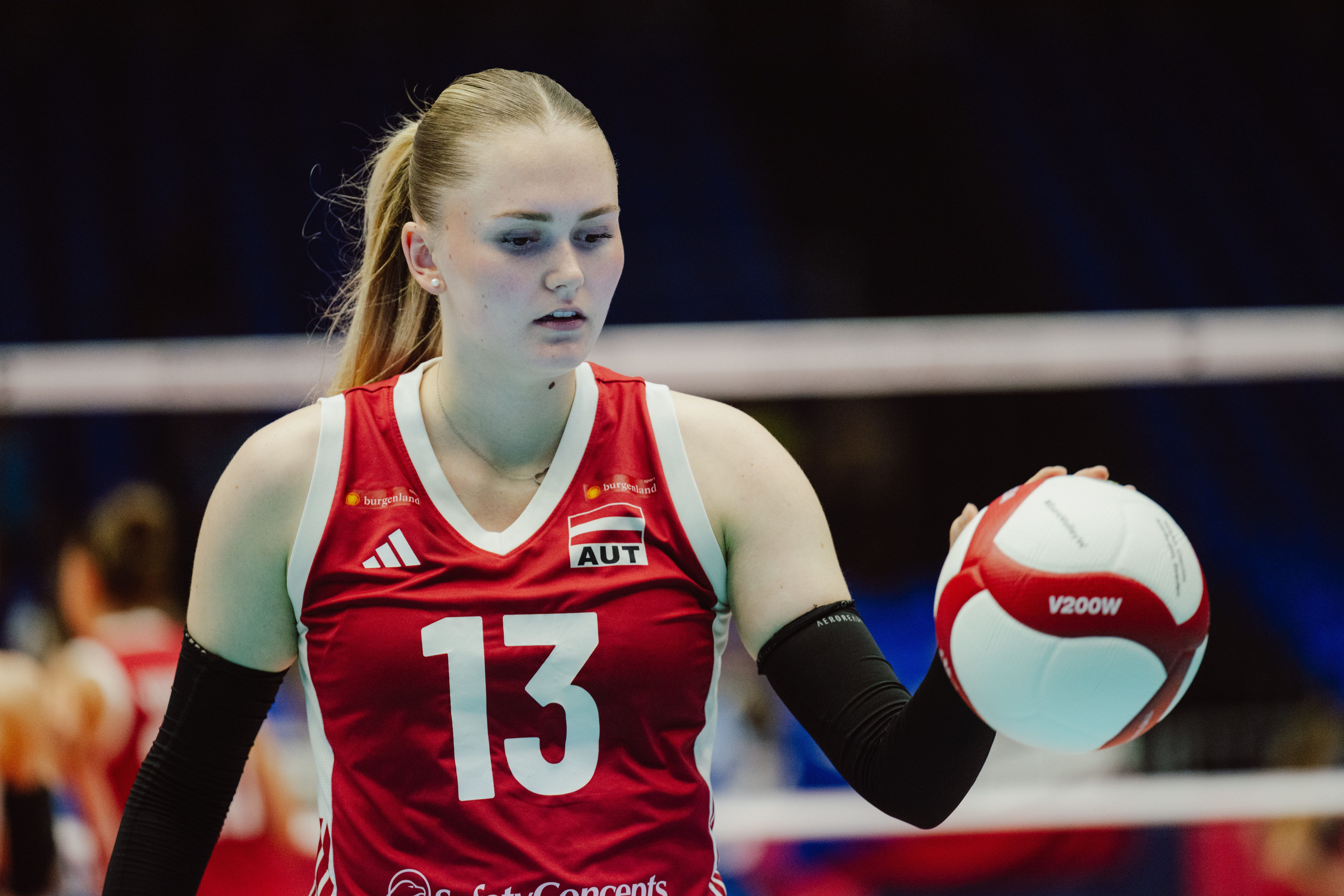 Eine Volleyballspielerin im roten Trikot hält einen Volleyball in der Hand.