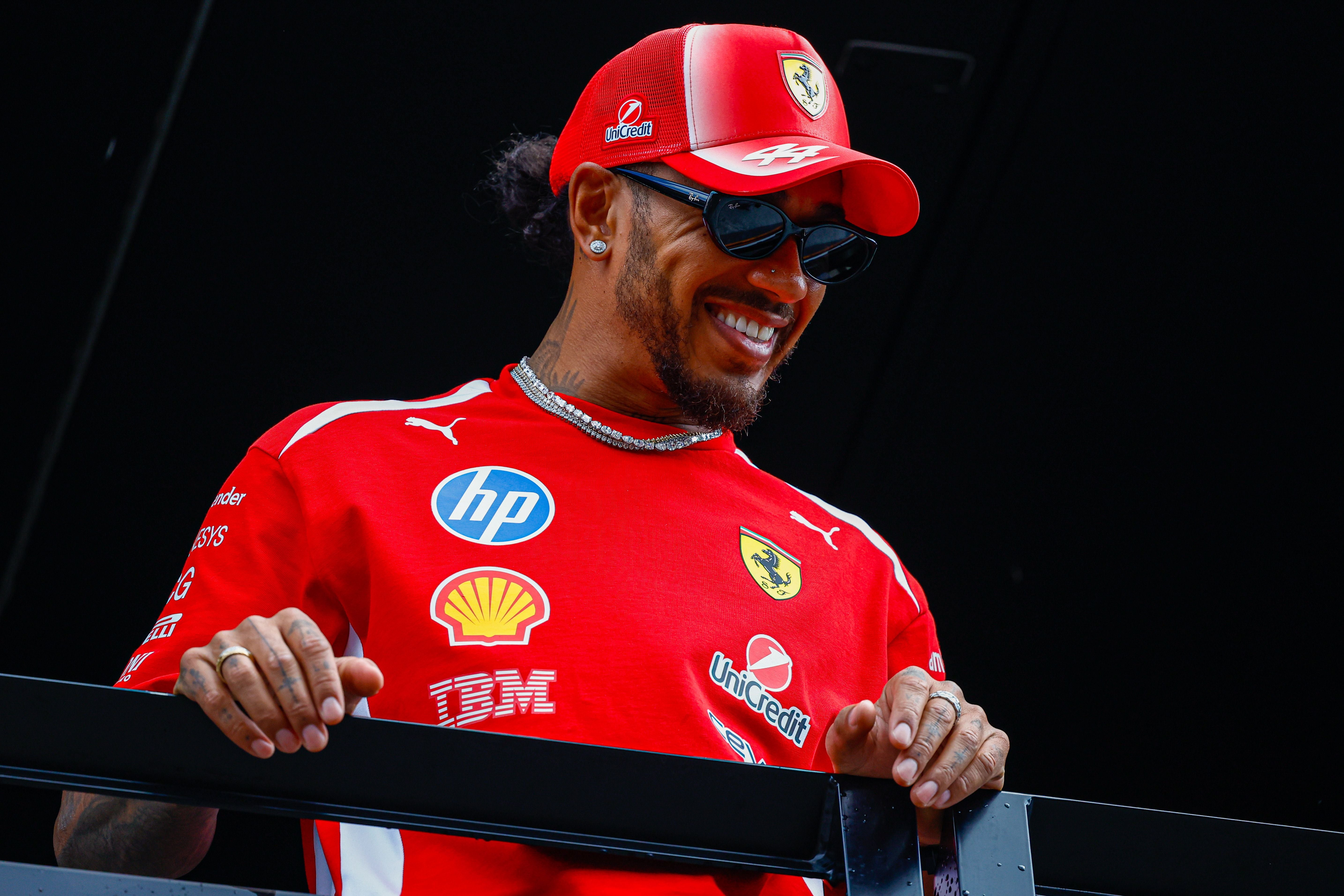 Ein Mann mit Ferrari-Shirt und -Kappe lächelt und steht hinter einem Geländer.