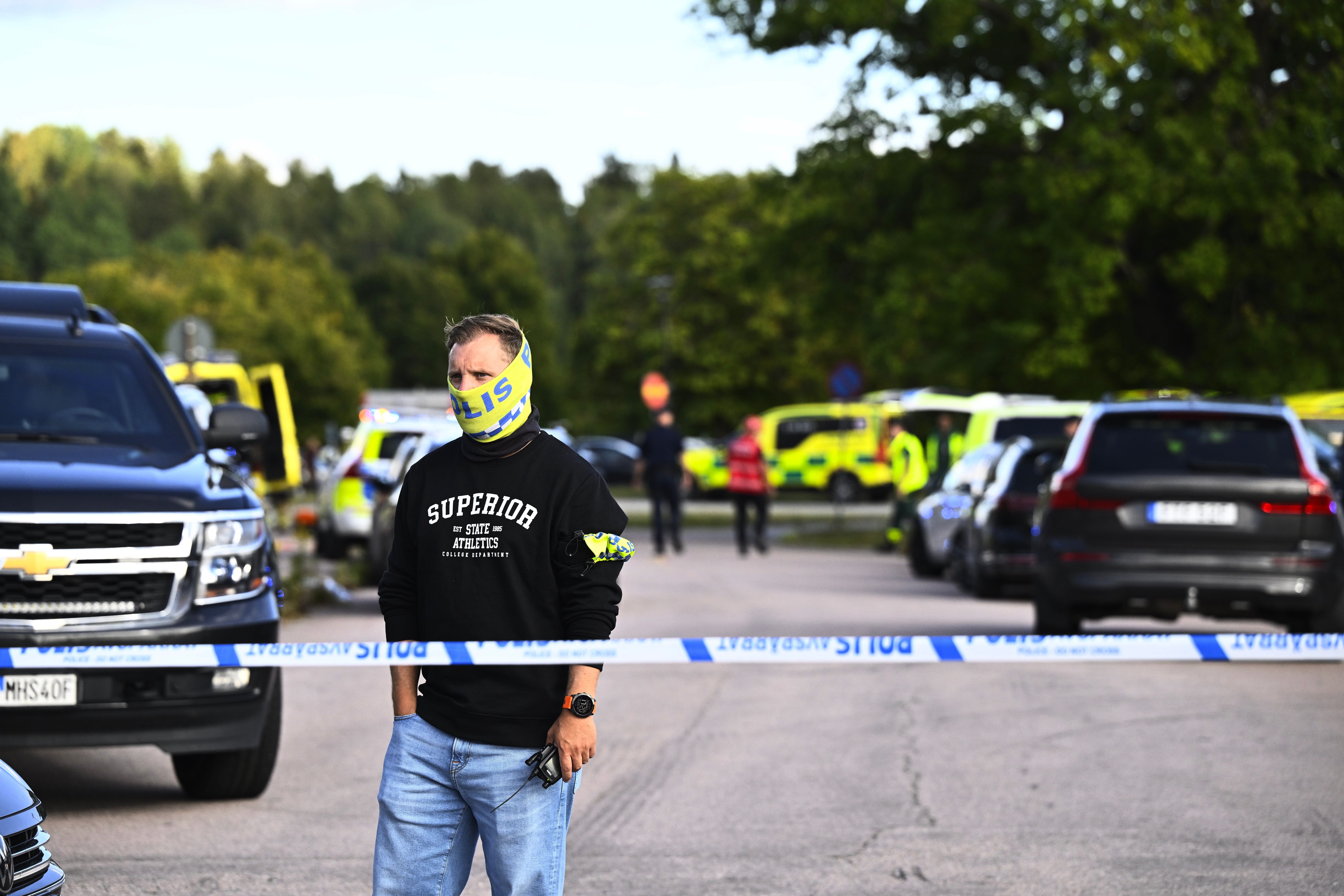 Ein Mann mit Polizei-Schal steht an einer Absperrung, im Hintergrund Einsatzfahrzeuge.