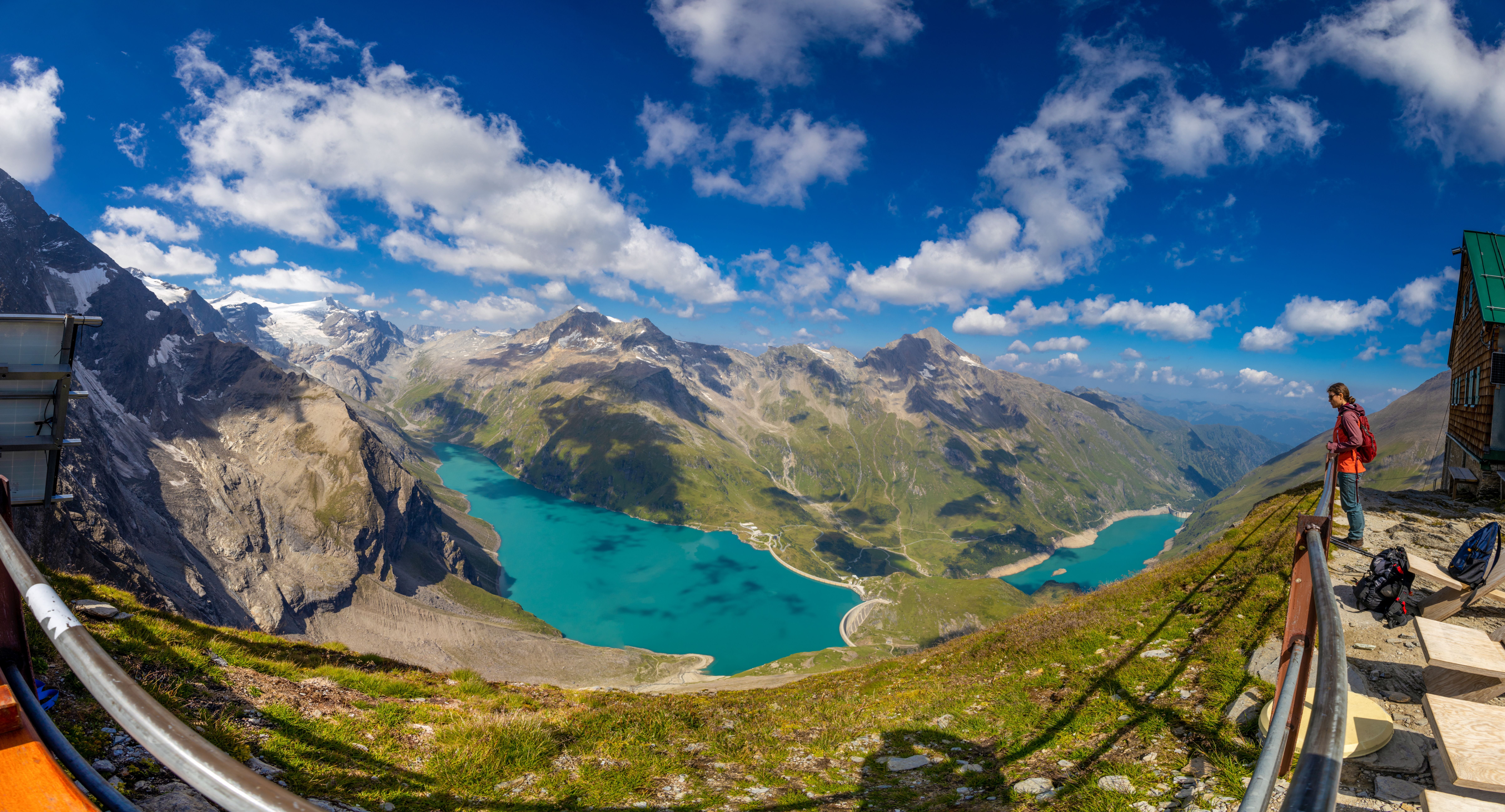 Panorama von Hochgebirge, türkisfarbenem Stausee und Wanderer am Heinrich-Schwaiger-Haus bei Kaprun.