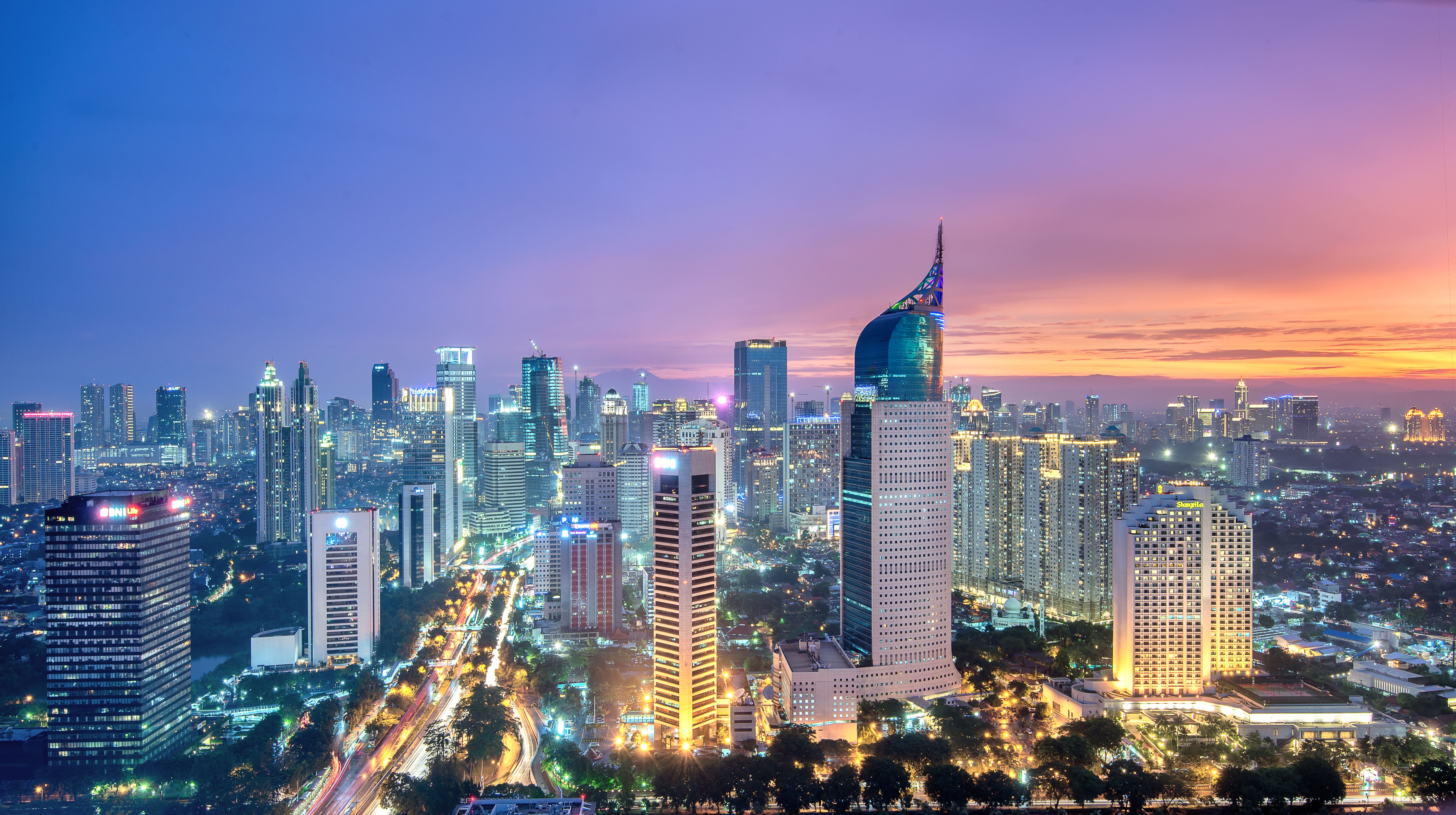 Jakartas Skyline bei Sonnenuntergang mit beleuchteten Hochhäusern und farbigem Himmel.