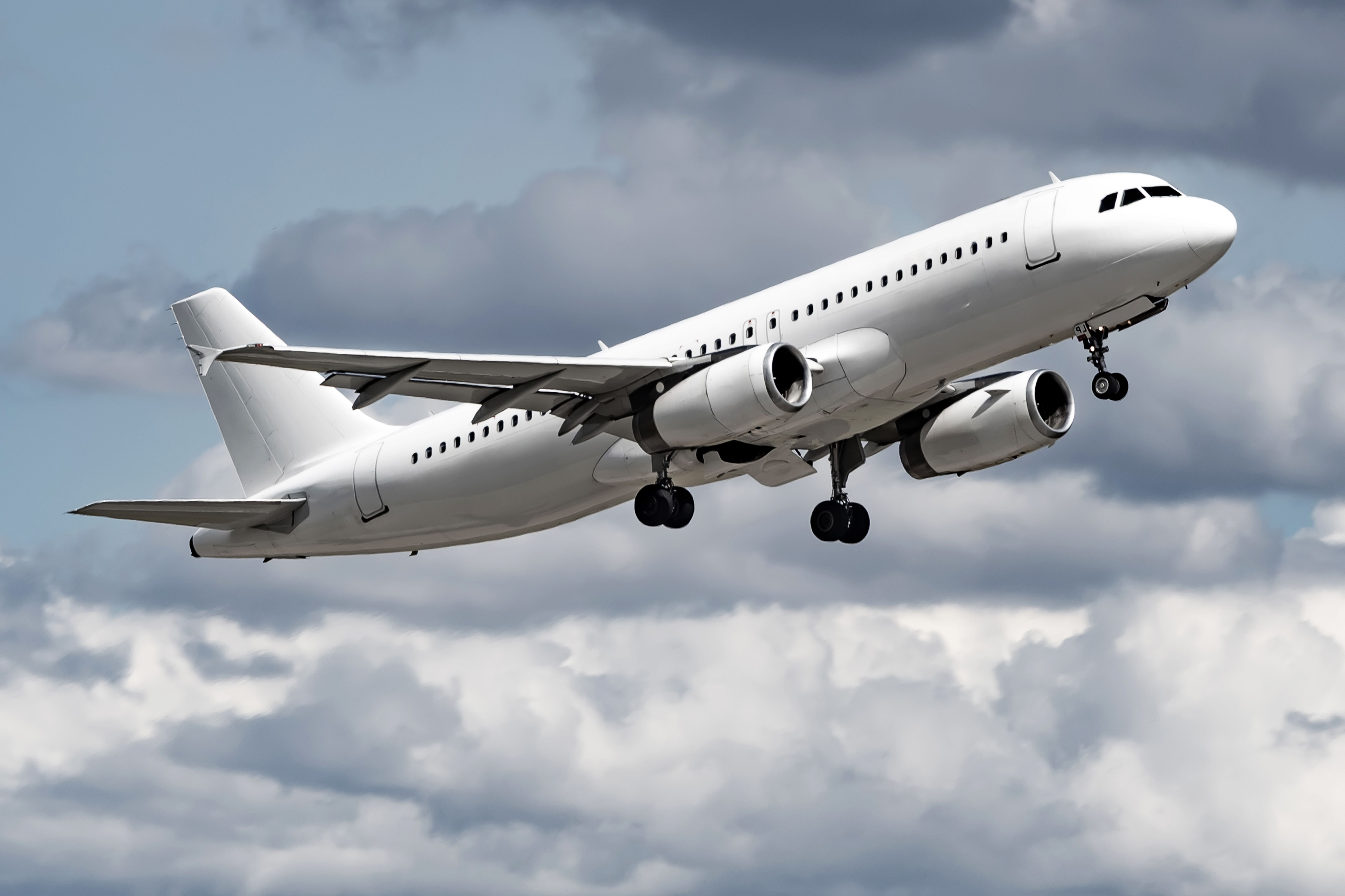 Weißes Passagierflugzeug fliegt vor bewölktem Himmel.
