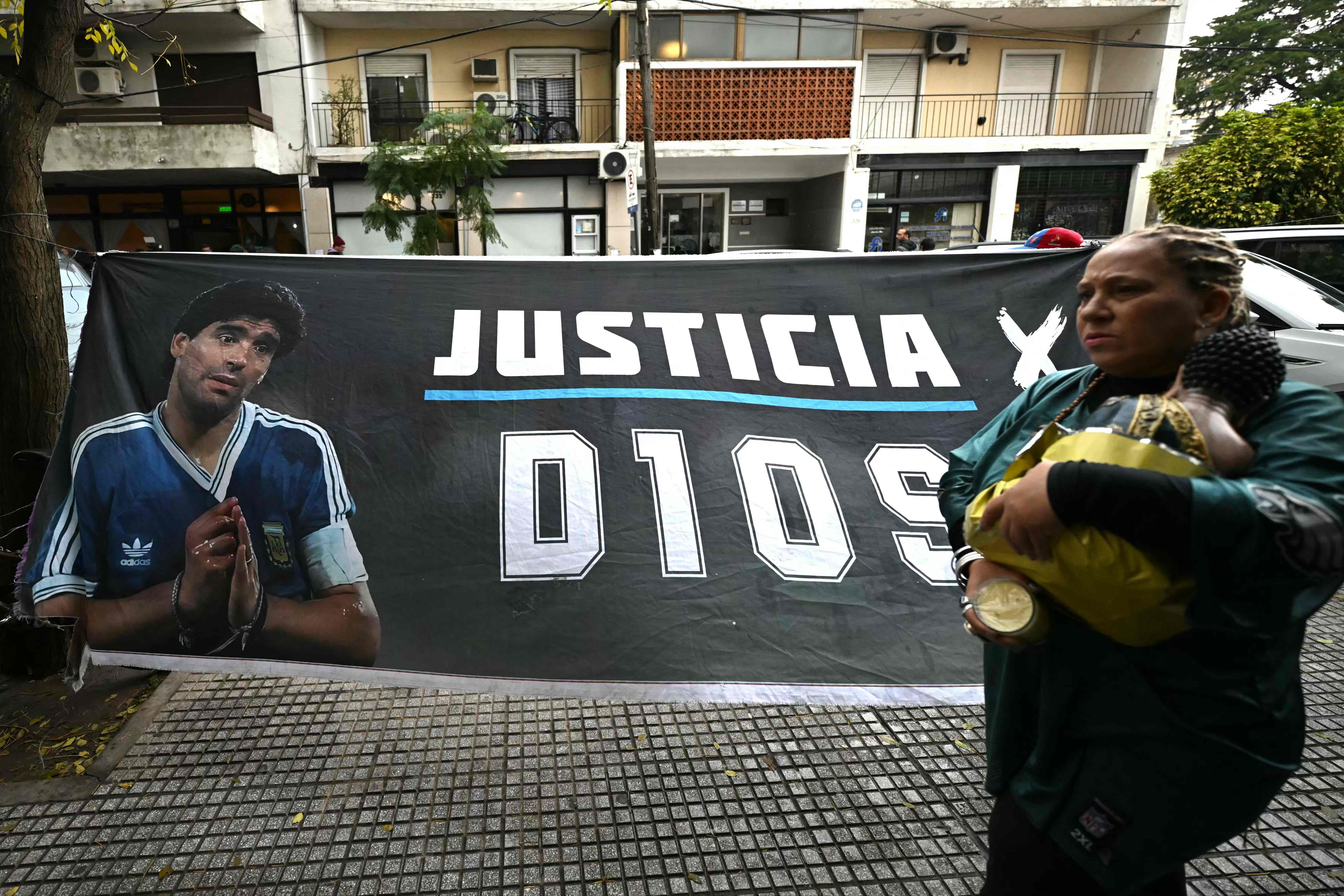 Frau läuft an Banner mit Maradona-Bild und der Aufschrift „Justicia x D10S“ vorbei.