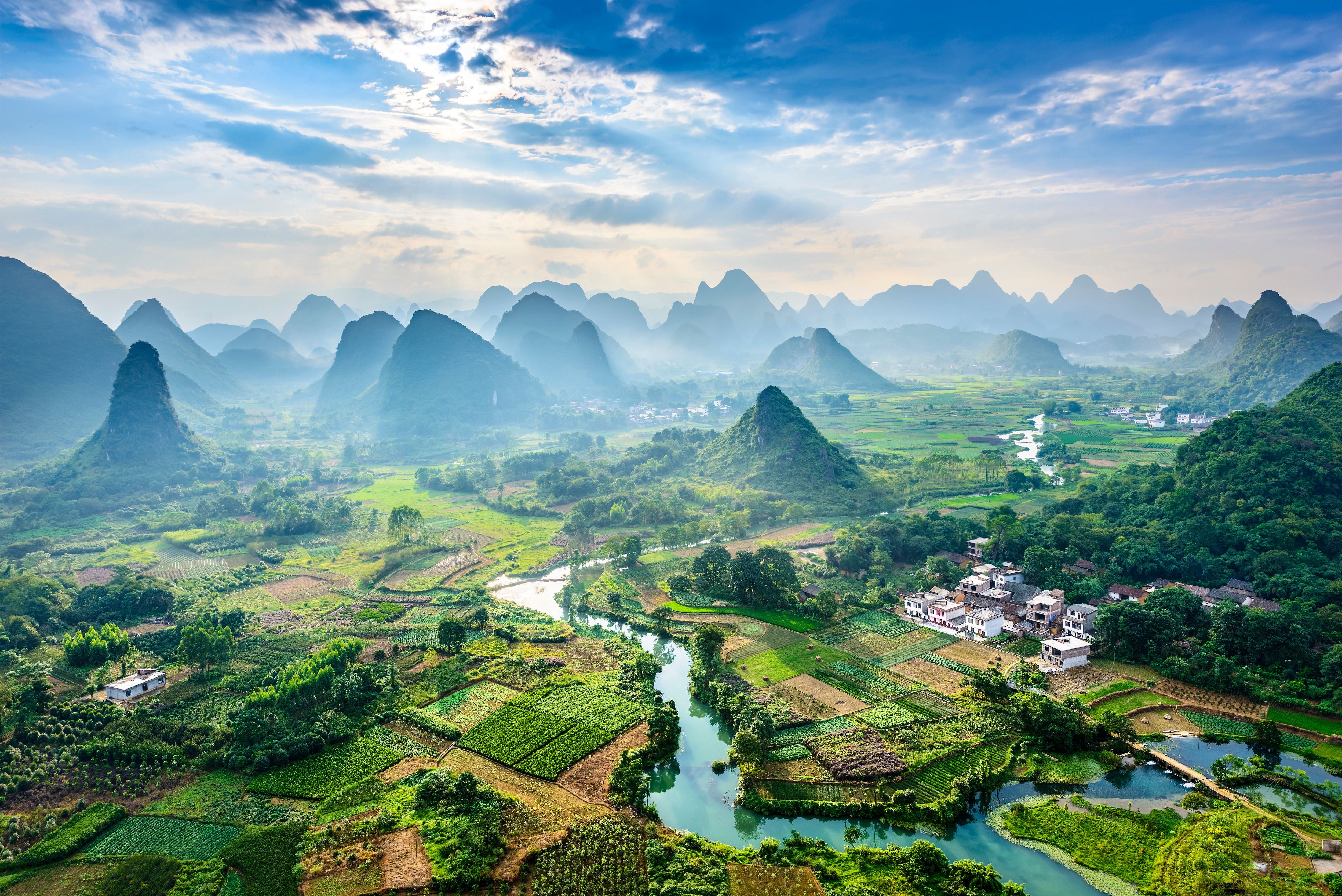 Landschaft mit Karstbergen, Feldern, Fluss und Dorf nahe Guilin, China, unter blauem Himmel.