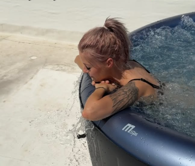 Frau mit Tattoo lehnt am Rand eines aufblasbaren Whirlpools im Freien.