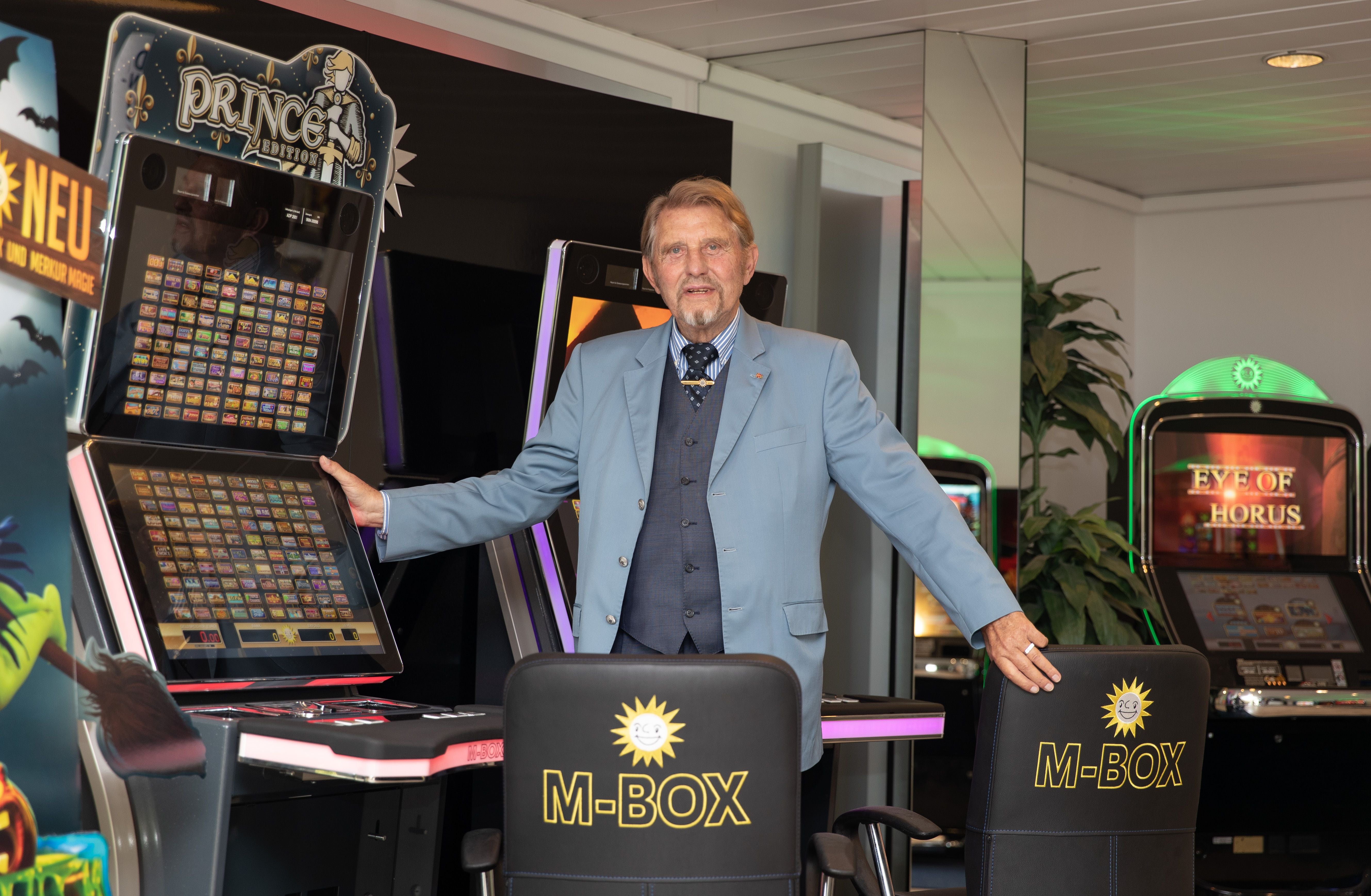 Ein älterer Mann im Anzug steht vor Spielautomaten im Ausstellungsraum einer Spielhalle.