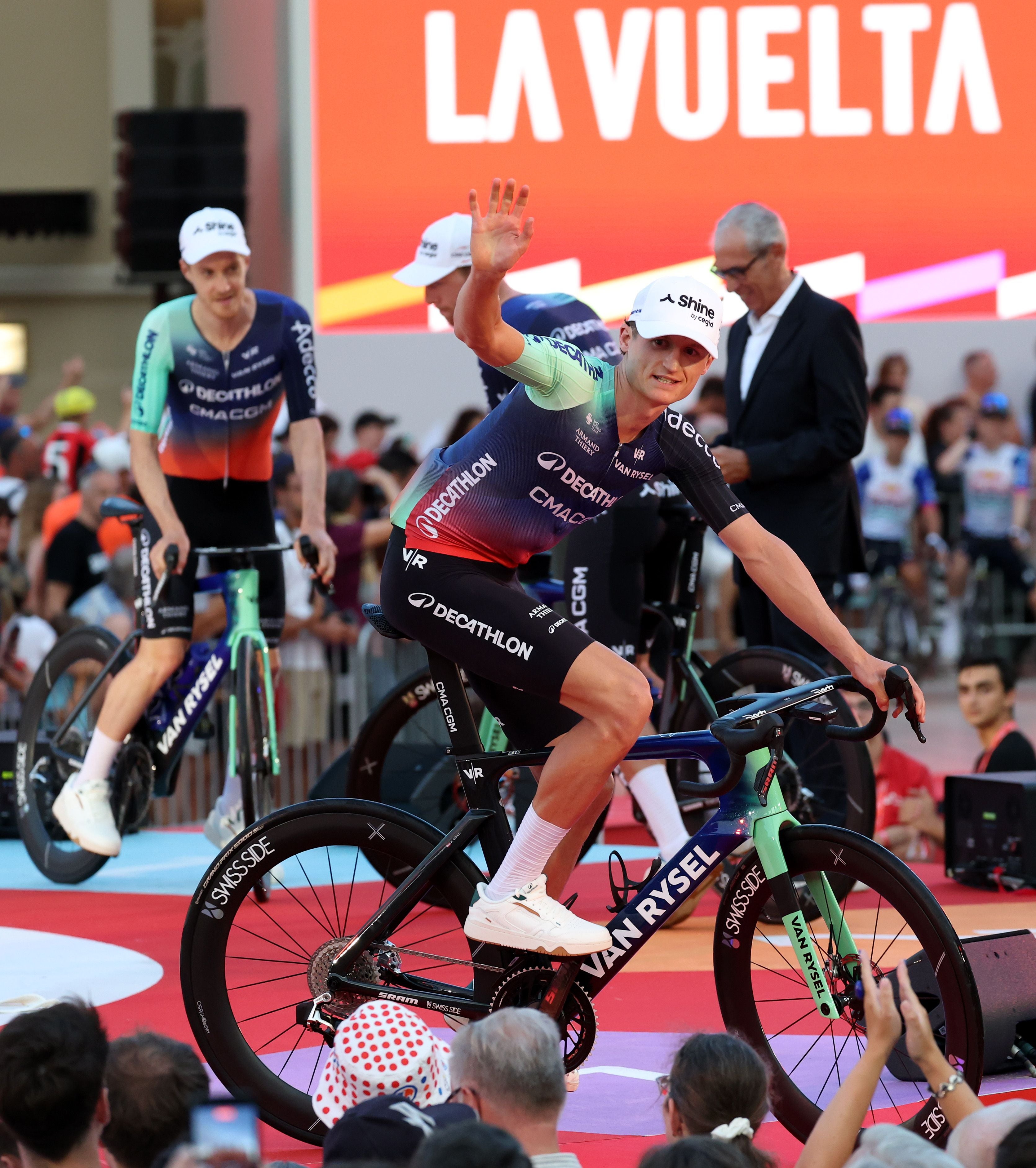 Ein Radrennfahrer winkt beim Teampräsentationsevent der La Vuelta 2026 in Monaco dem Publikum zu.