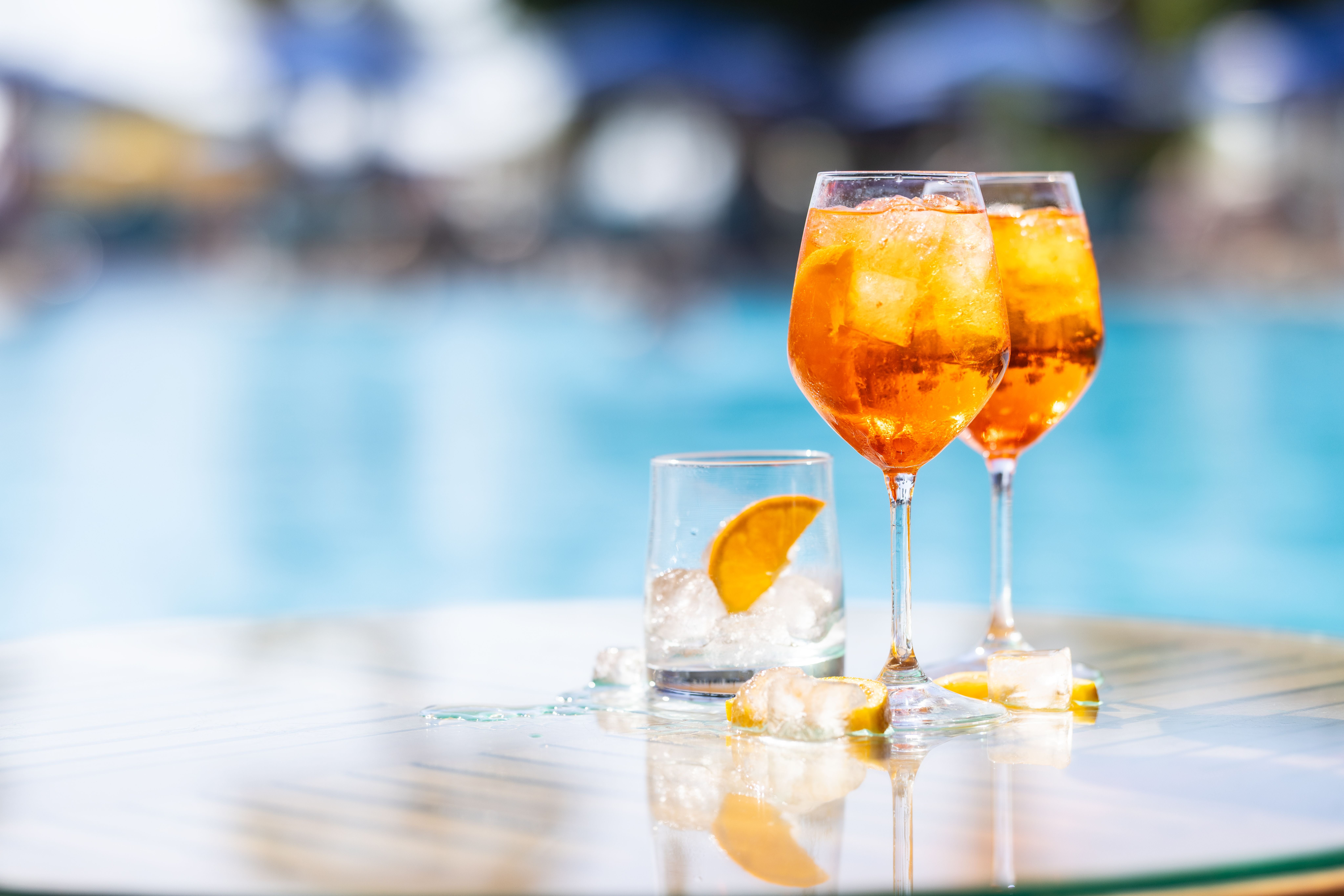 Zwei Aperol Spritz und ein Glas mit Eis und Orange auf einem Tisch am Pool.