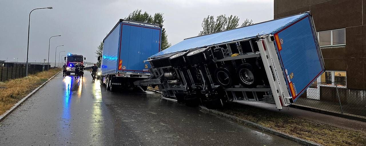 Ein umgekippter Lkw-Anhänger liegt neben einer nassen Straße, Feuerwehr ist vor Ort.