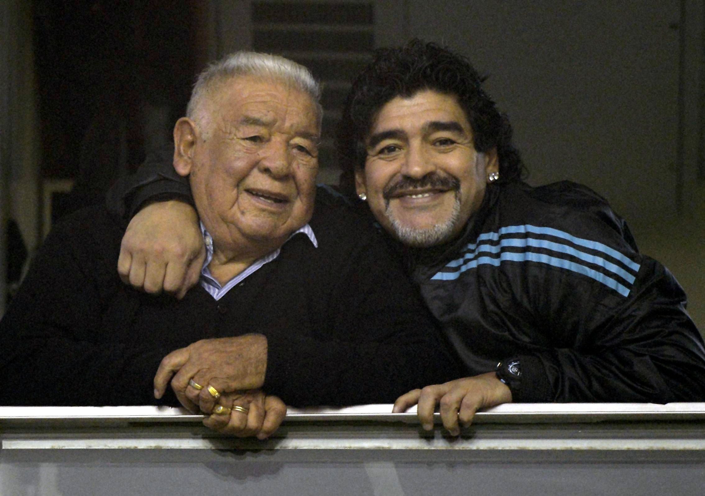 Zwei Männer umarmen sich und lächeln in eine Kamera, im Hintergrund unscharfes Stadion.