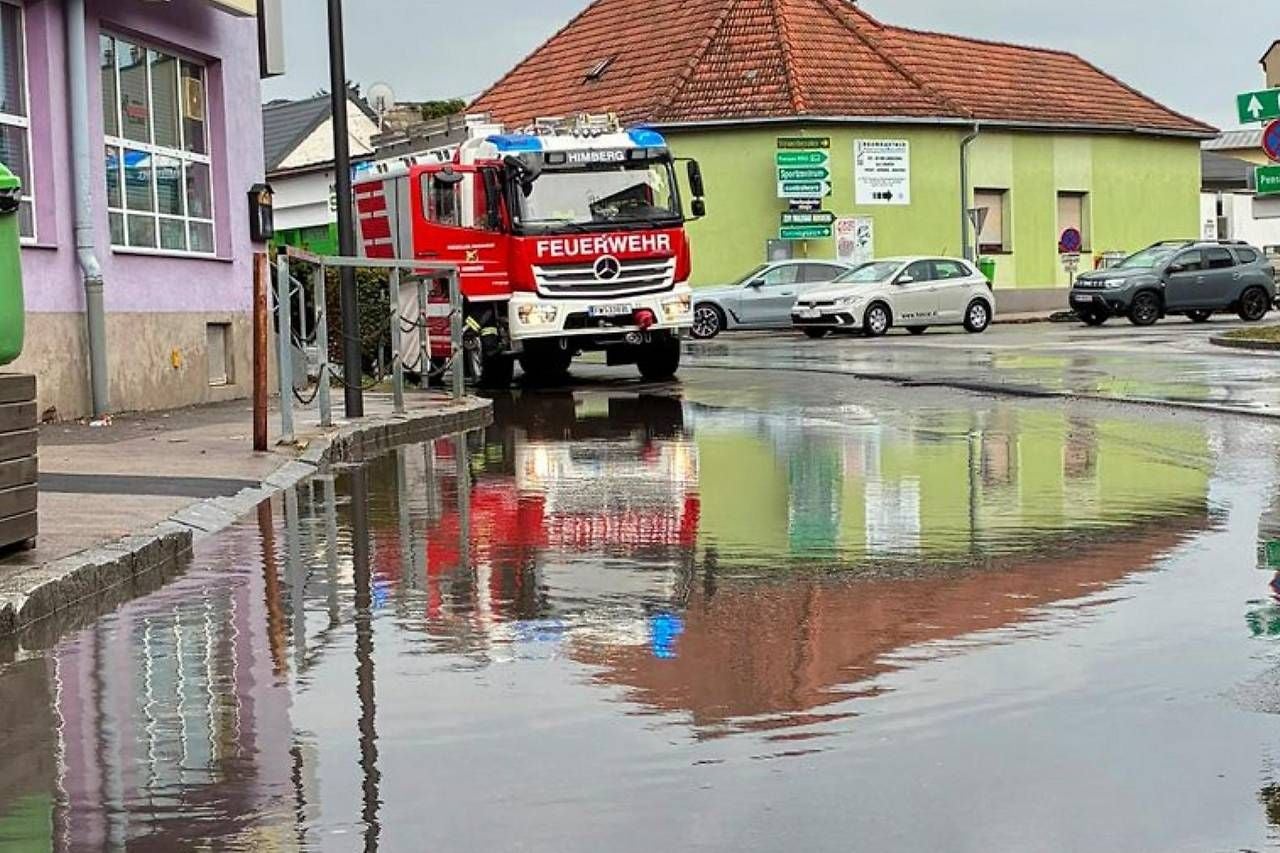 Ein Feuerwehrwagen steht bei Überschwemmung auf einer nassen Straße in einer Stadt.