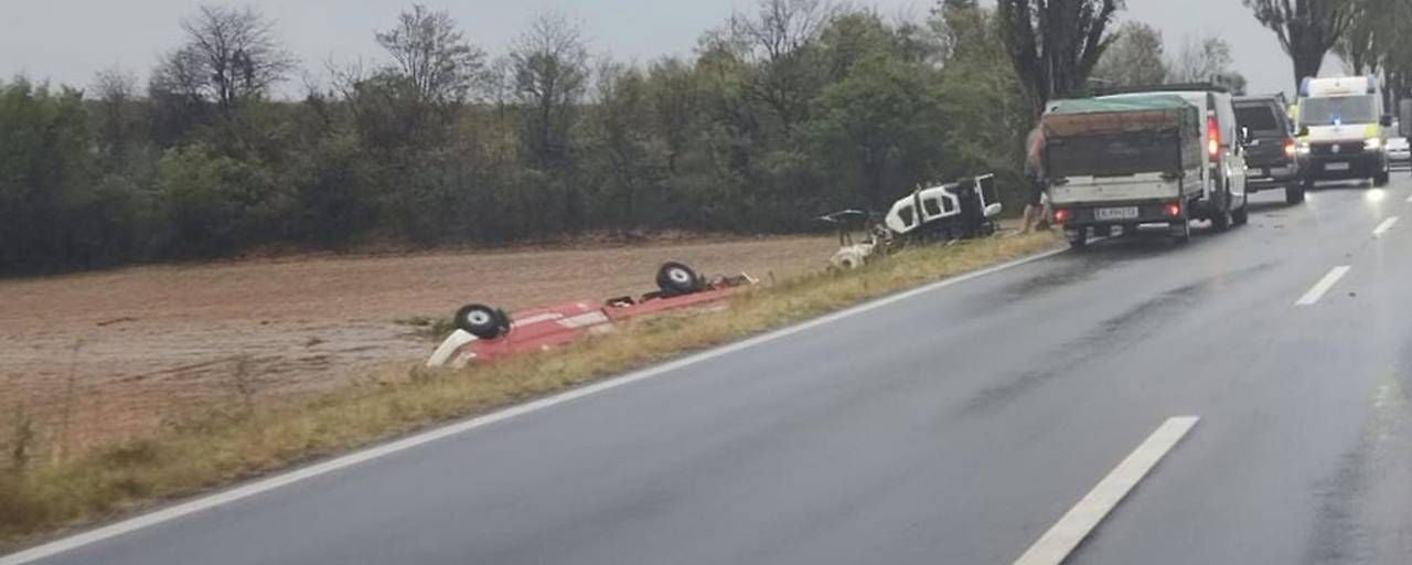Zwei umgekippte Fahrzeuge liegen neben einer regennassen Landstraße, Rettungsfahrzeuge sind vor Ort.