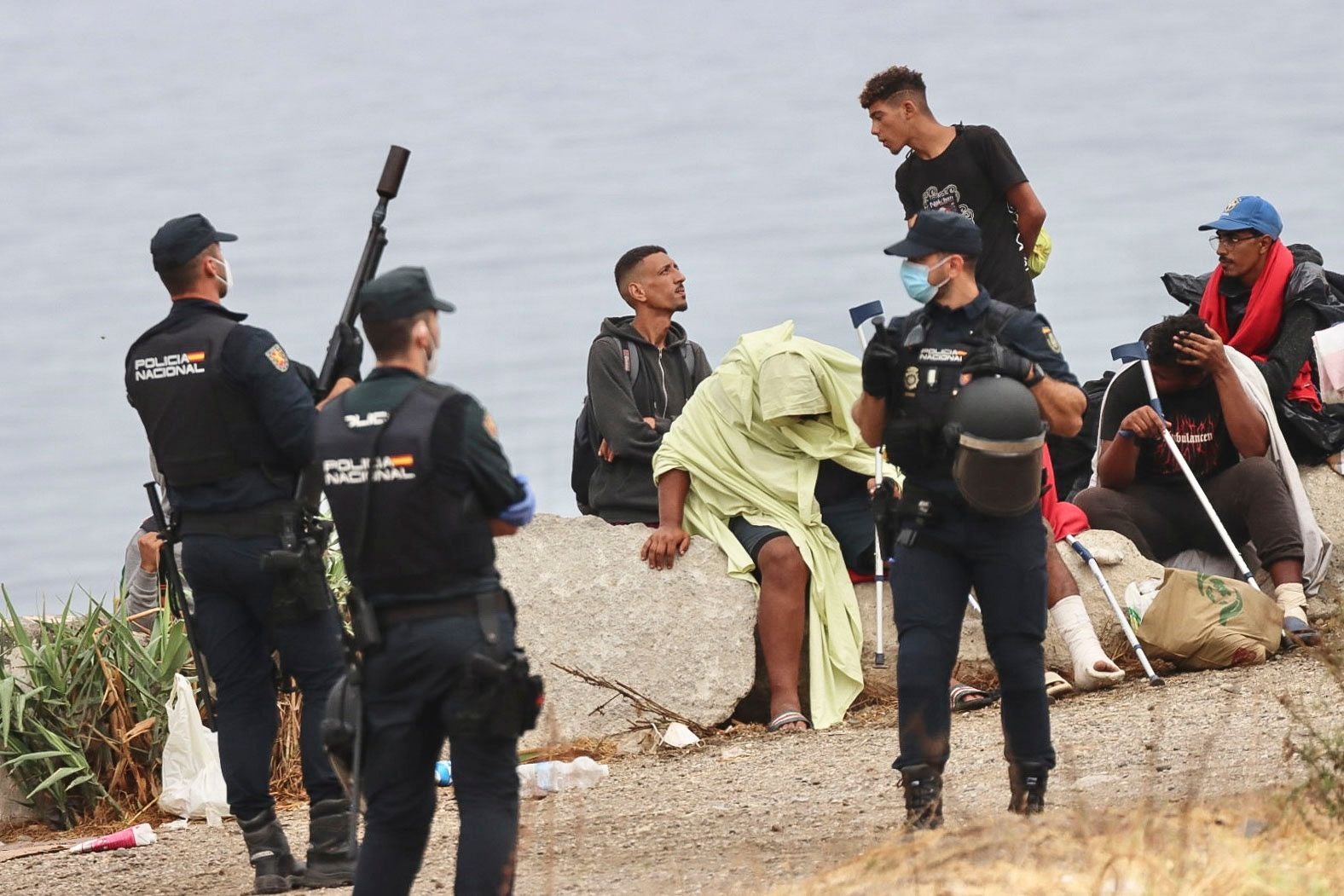 Mehrere Polizisten bewachen eine Gruppe Migranten am Strand von El Trampolin in Ceuta, Spanien.