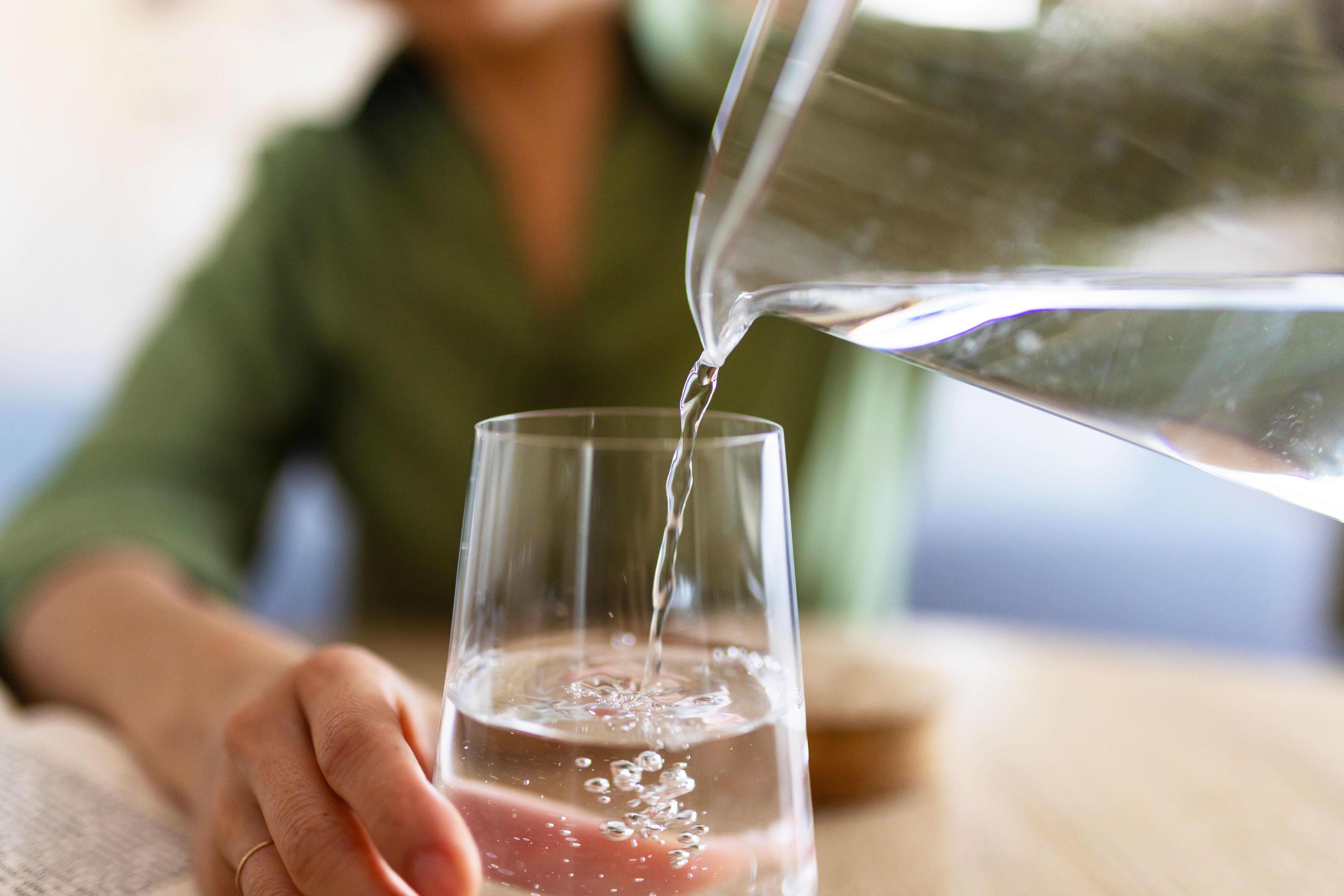 Nahaufnahme einer Person, die Wasser aus einem Krug in ein Glas gießt.