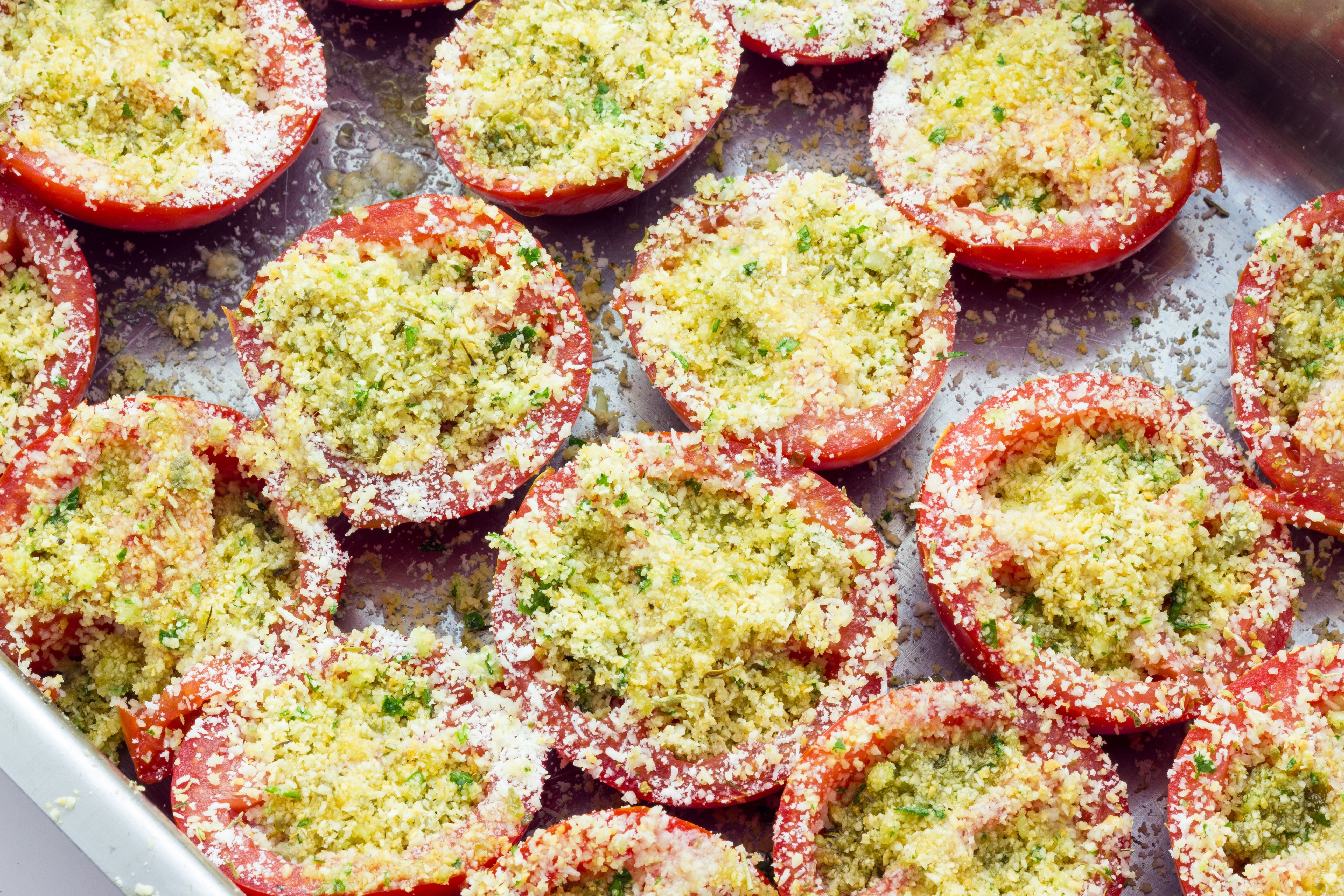 Halbierte Tomaten mit Kräutern und Semmelbröseln in einer Auflaufform für Tomatengratin.