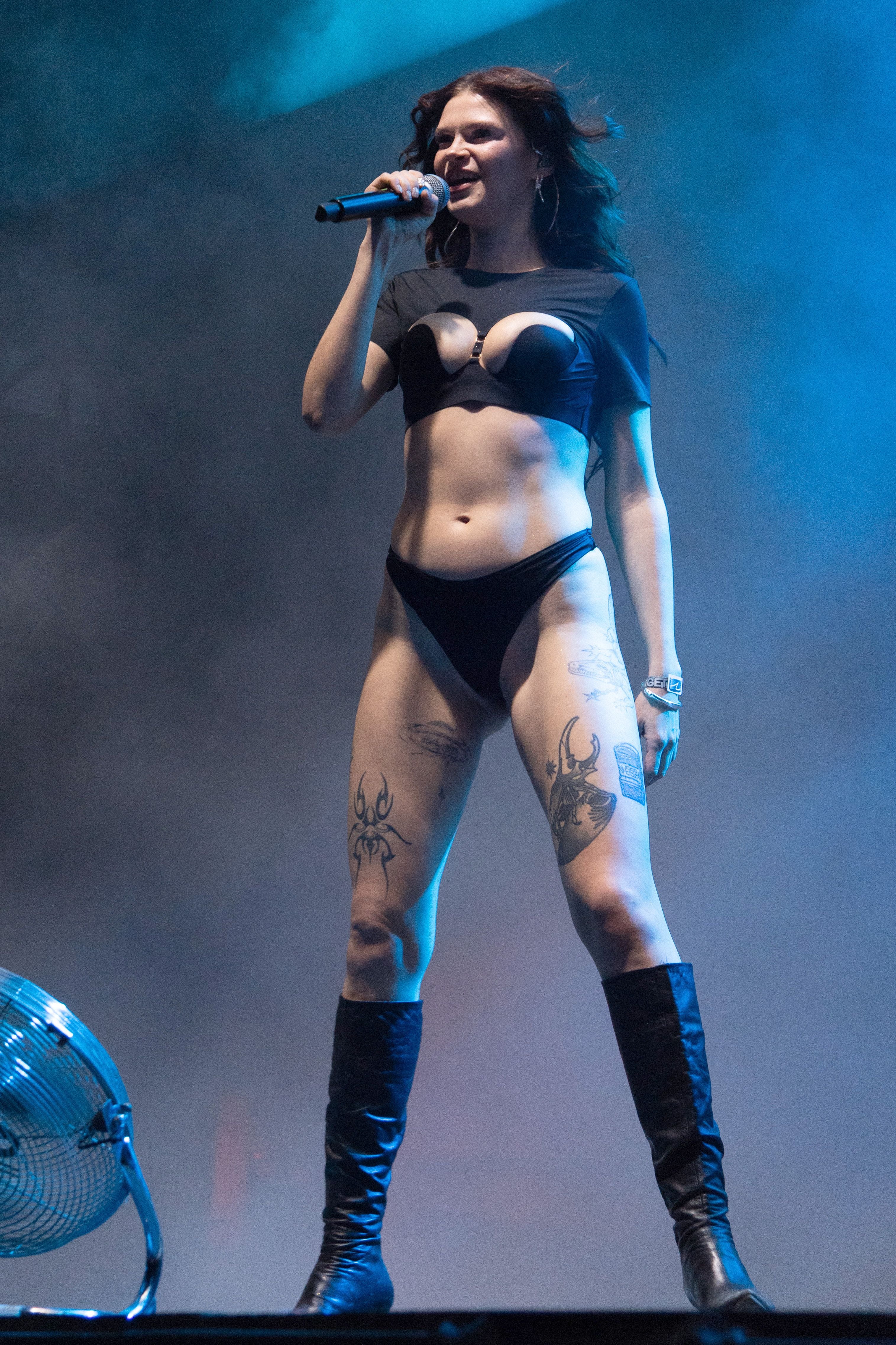 Eine Sängerin mit Tattoos und schwarzem Outfit tritt auf einer Bühne mit Mikrofon auf.
