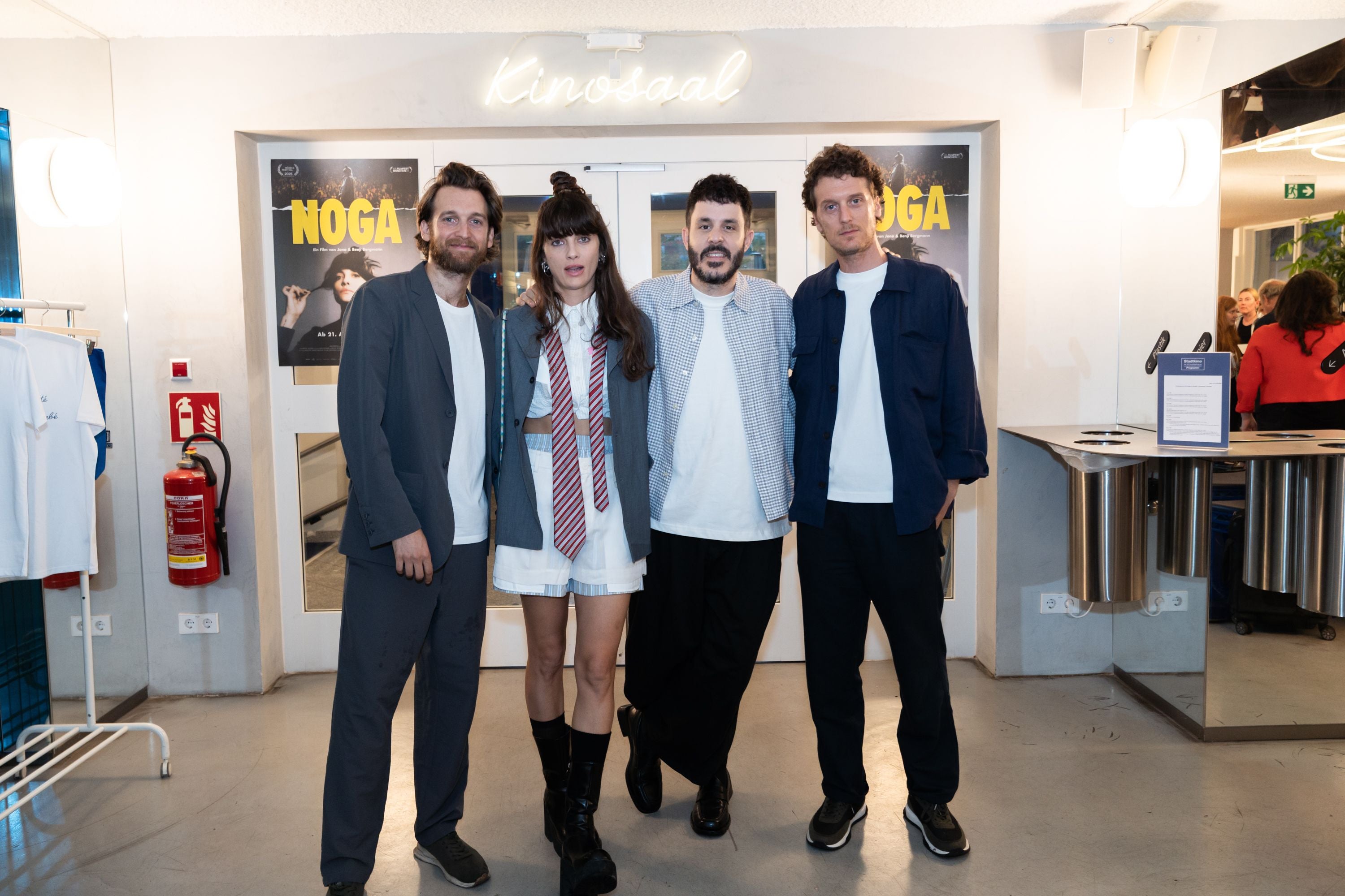 Vier Personen posieren bei der NOGA-Premiere vor einem Kinoeingang mit Filmpostern.