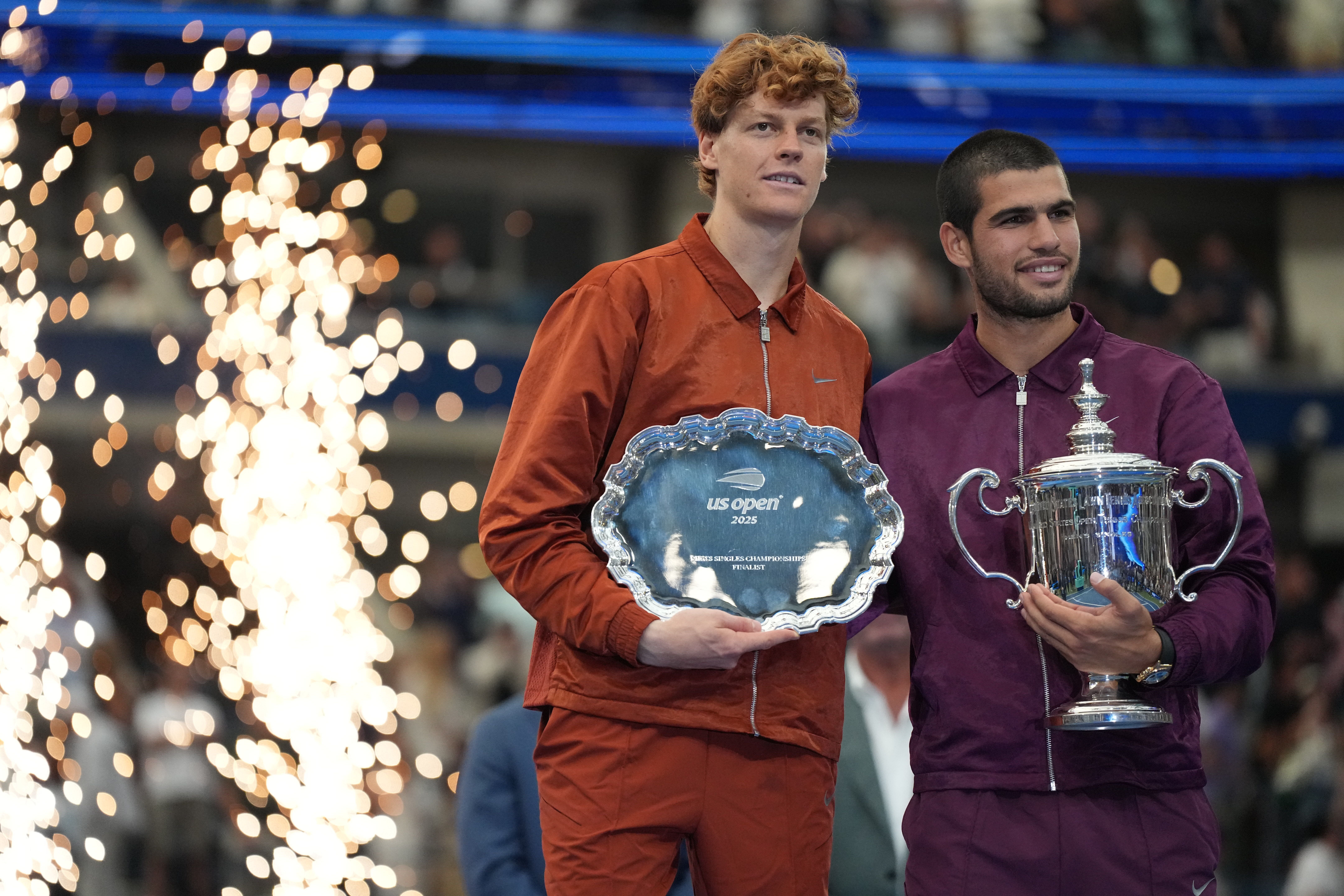Zwei Tennisspieler posieren nach dem US Open Finale 2025 mit Pokal und Silberteller auf dem Podium.