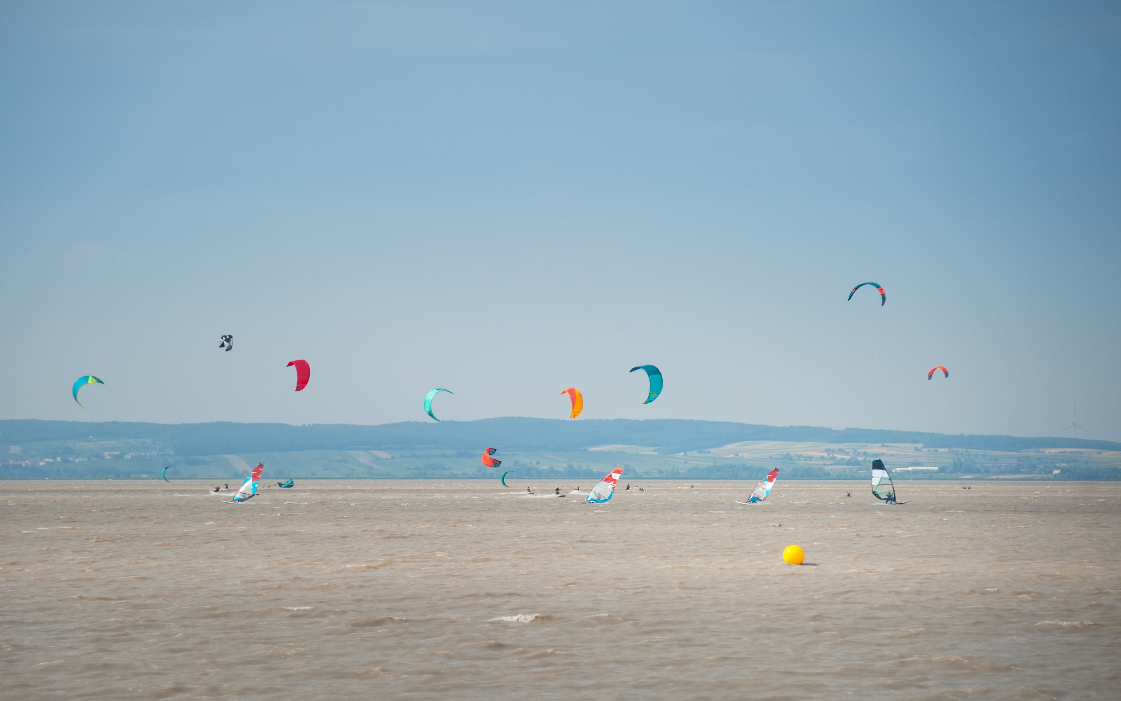 Mehrere Kitesurfer und Windsurfer auf dem Neusiedler See unter blauem Himmel.