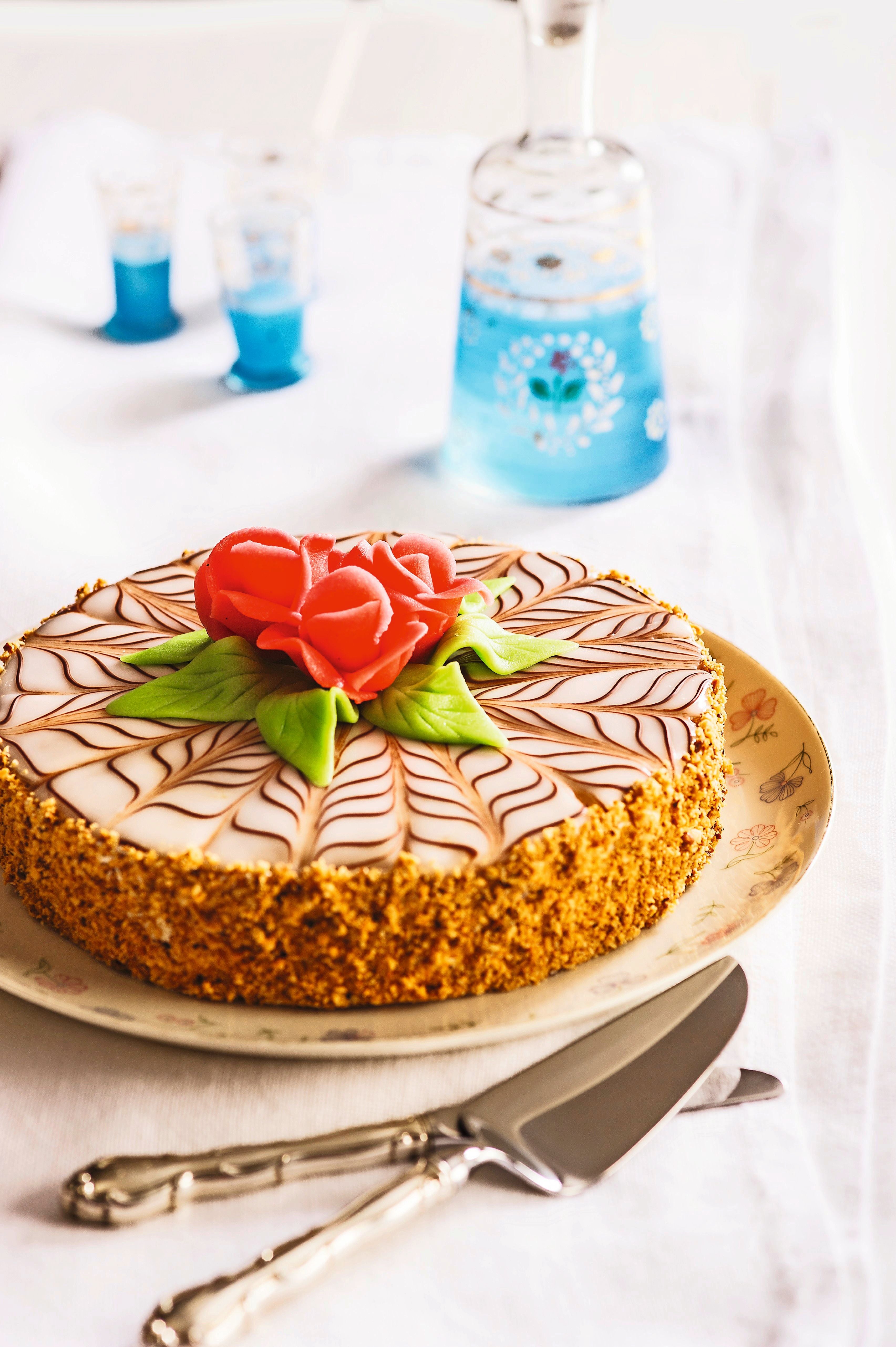 Esterhazytorte mit Zuckerglasur, dekoriert mit Marzipanrosen und grünen Blättern auf einem Teller.