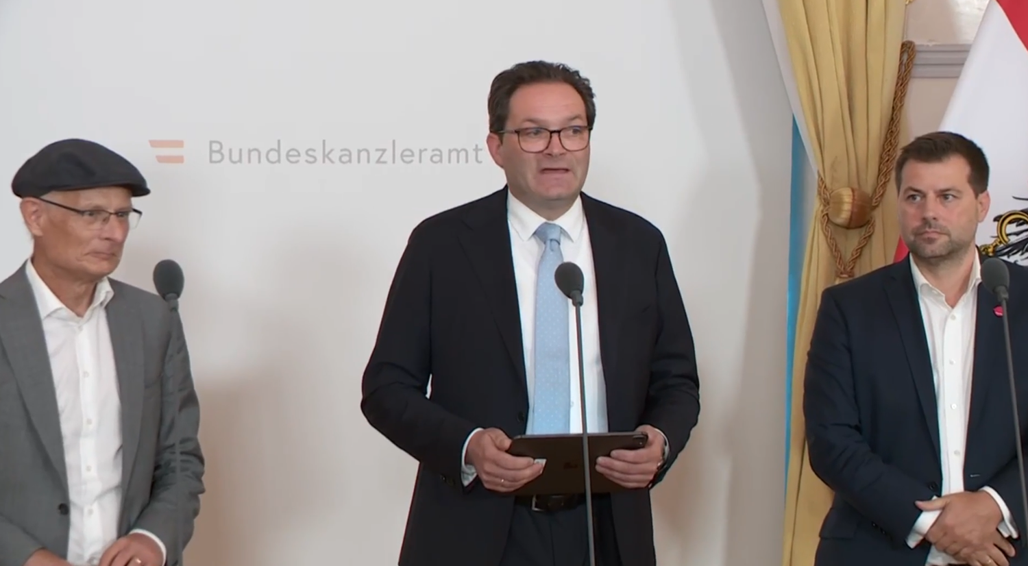 Drei Männer im Anzug stehen bei einer Pressekonferenz im Bundeskanzleramt.