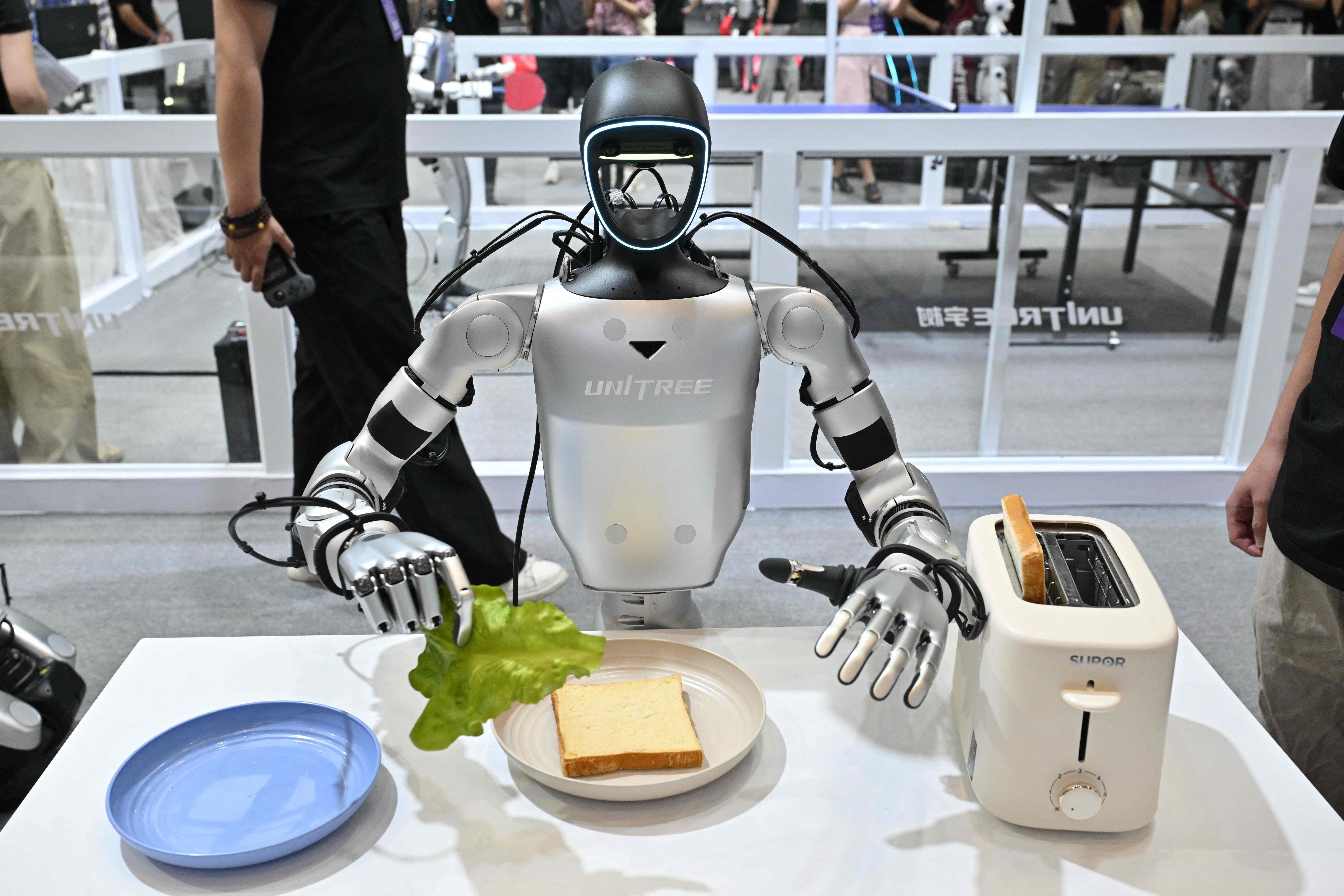 Ein humanoider Roboter bereitet bei einer Messe ein Sandwich mit Toast und Salat zu.