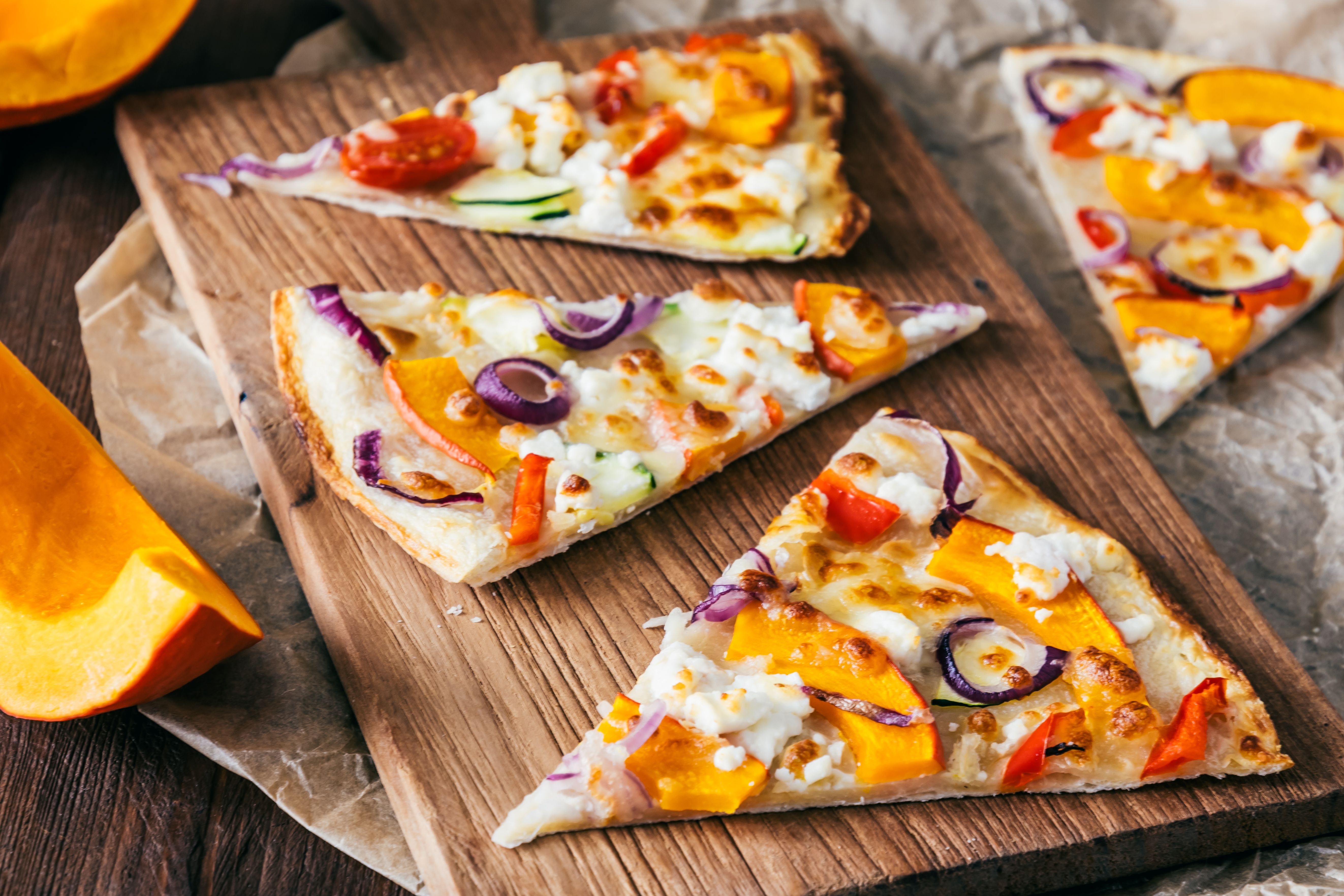 Stücke Flammkuchen mit Kürbis, roten Zwiebeln und Käse auf einem Holzbrett.