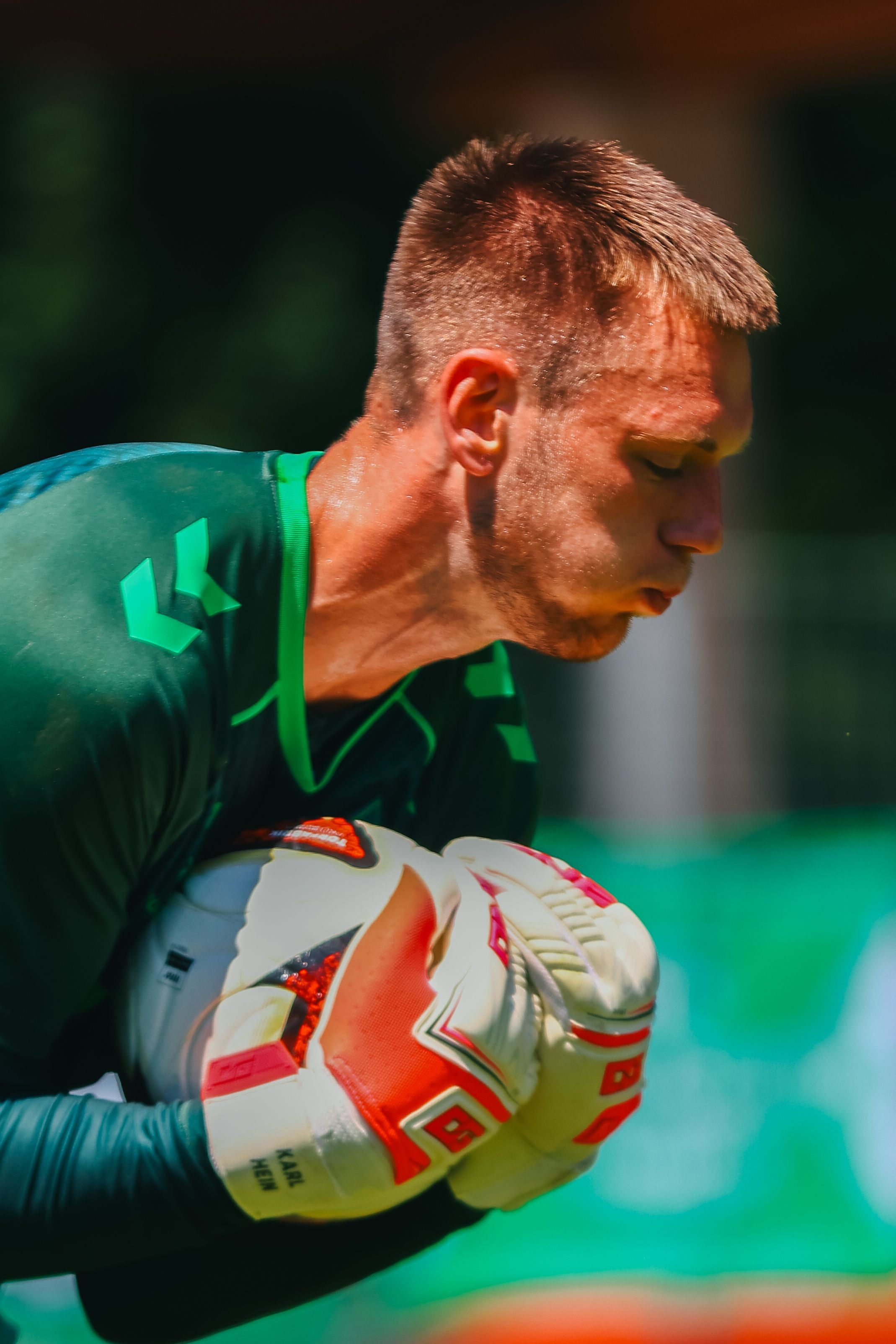Ein Torwart mit grünen Handschuhen hält einen Fußball fest beim Aufwärmen.