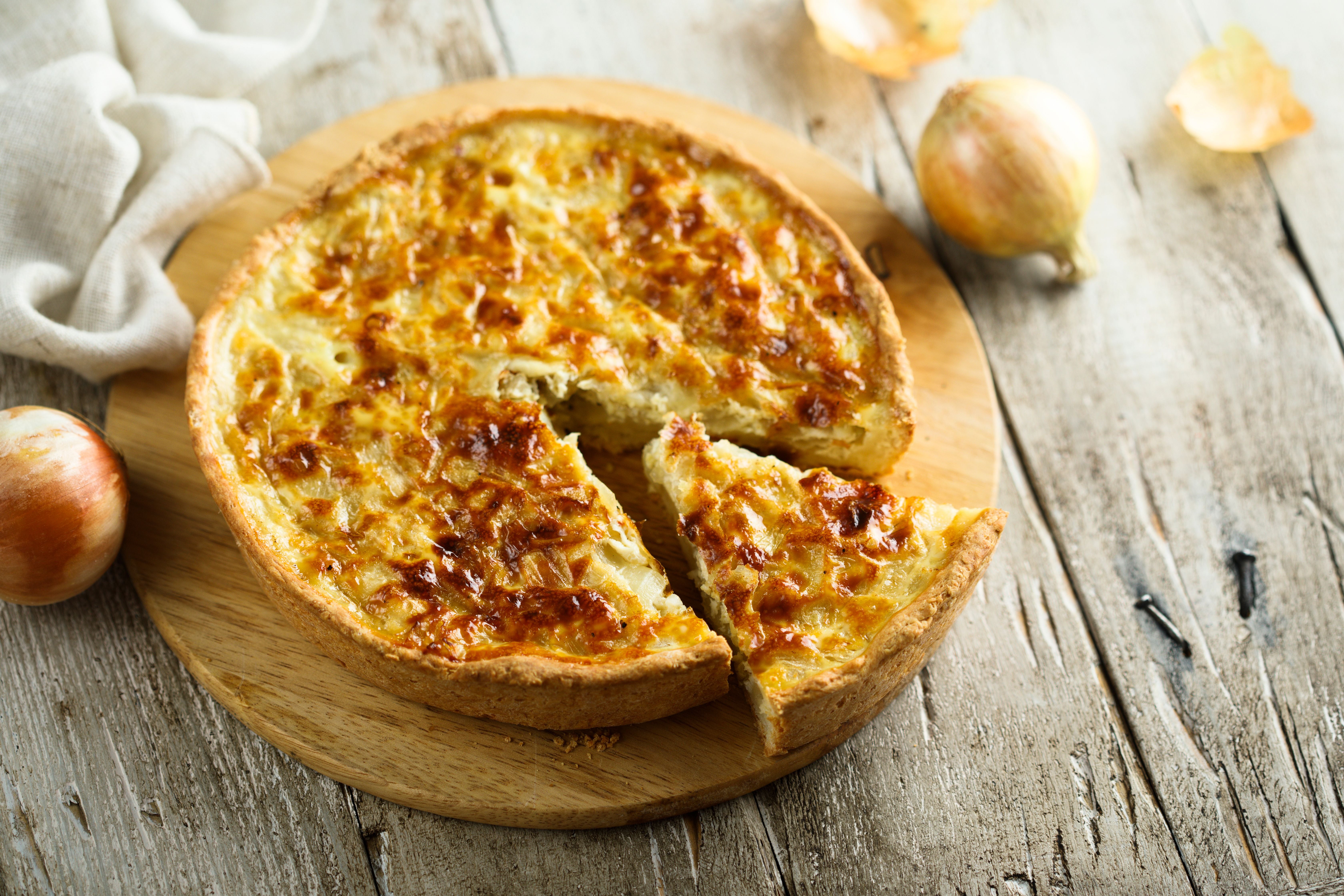 Hausgemachte Zwiebelquiche auf Holzbrett, ein Stück ist angeschnitten.