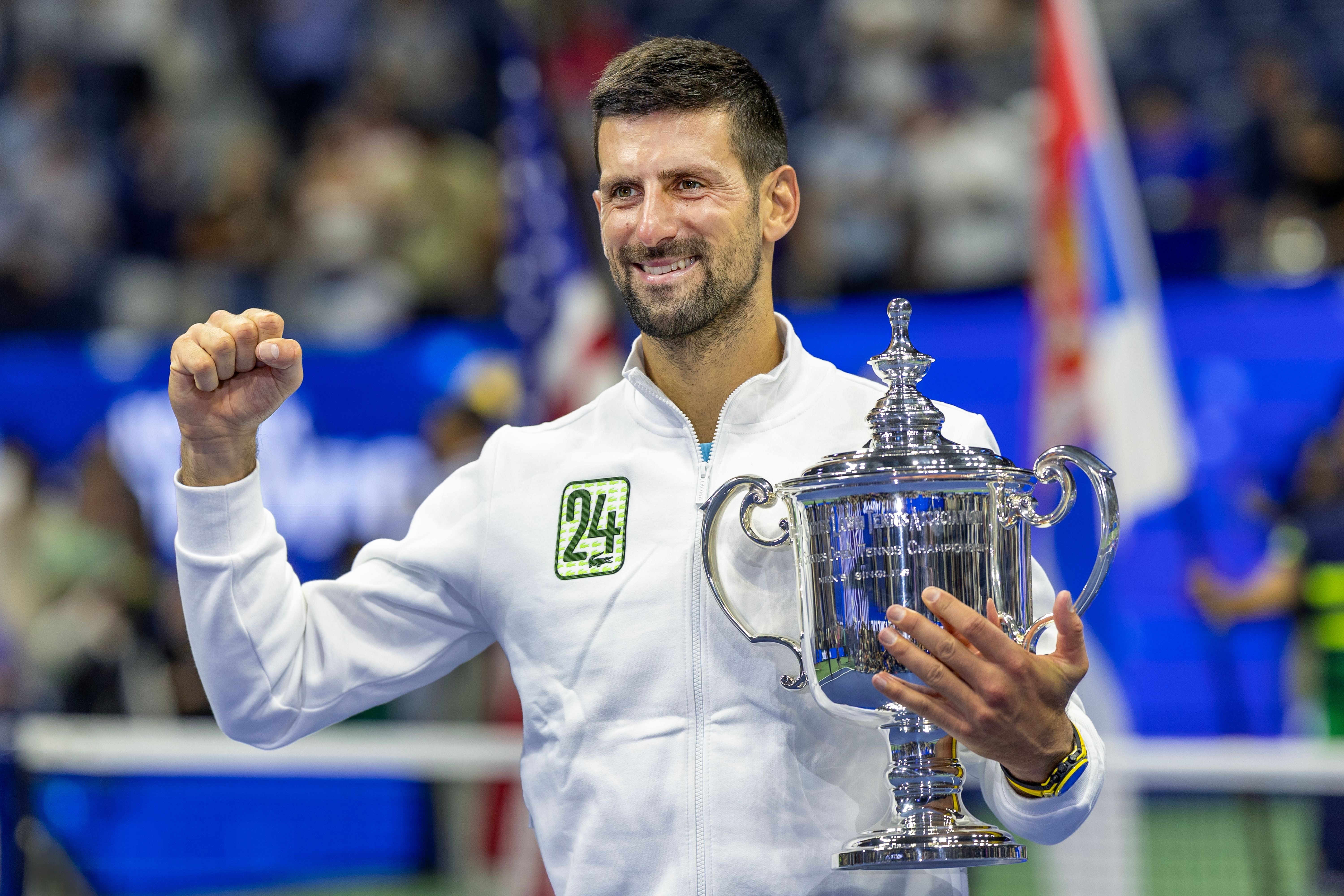 Novak Djokovic hält die US-Open-Trophäe und jubelt mit erhobener Faust.