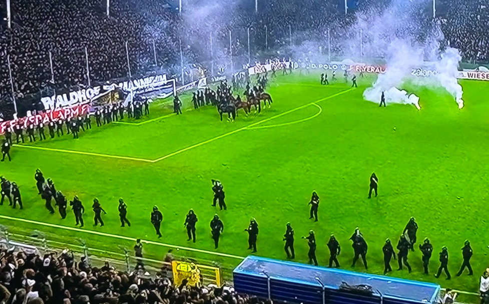 Polizeikette und berittene Polizei sichern nach Pyro-Einsatz ein Fußballfeld im Stadion.