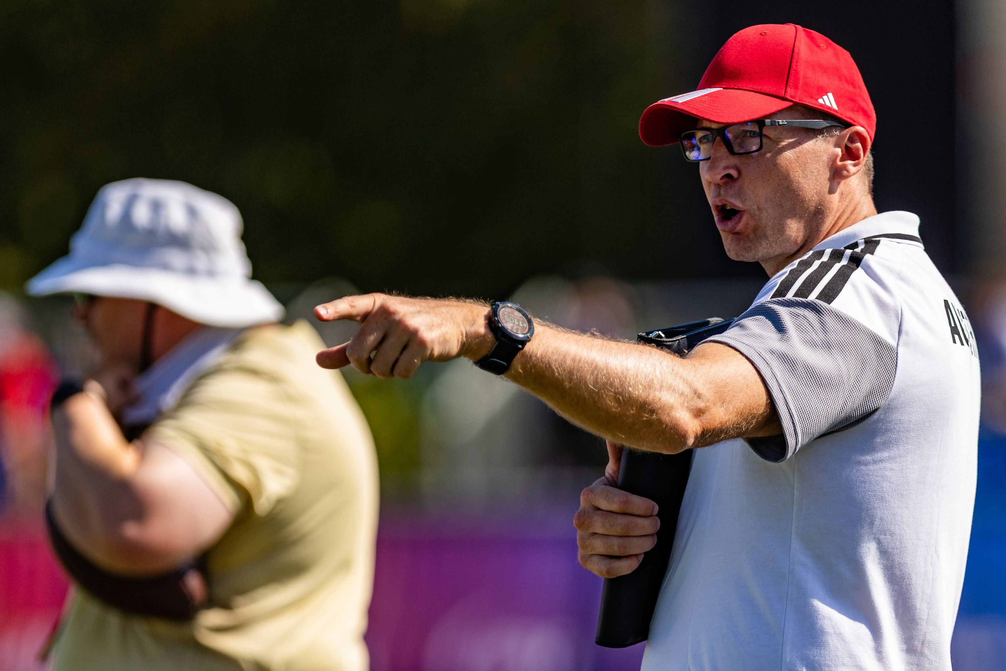 Ein Trainer mit roter Kappe zeigt energisch in eine Richtung bei einem Flag Football-Spiel.