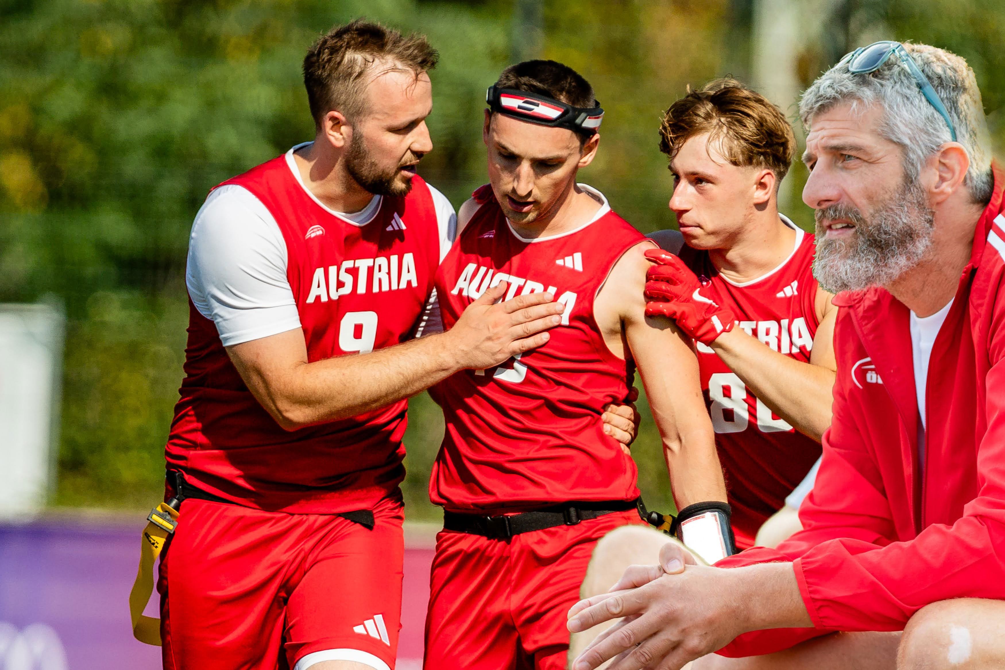 Drei Flag Football Spieler aus Österreich unterstützen einen verletzten Mitspieler, ein Trainer sitzt daneben.