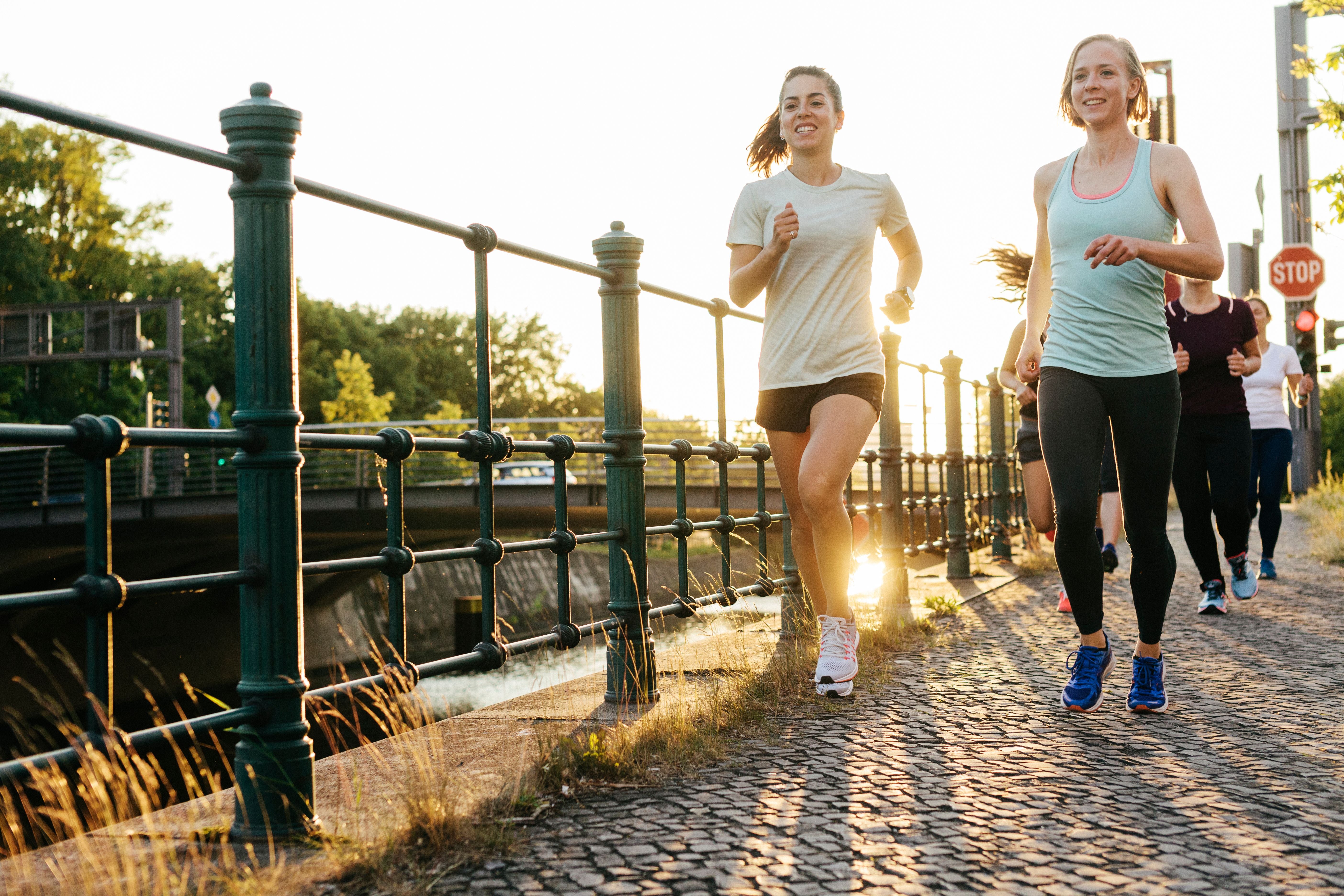 Mehrere Frauen joggen gemeinsam auf einem gepflasterten Weg entlang eines Kanals in der Stadt.